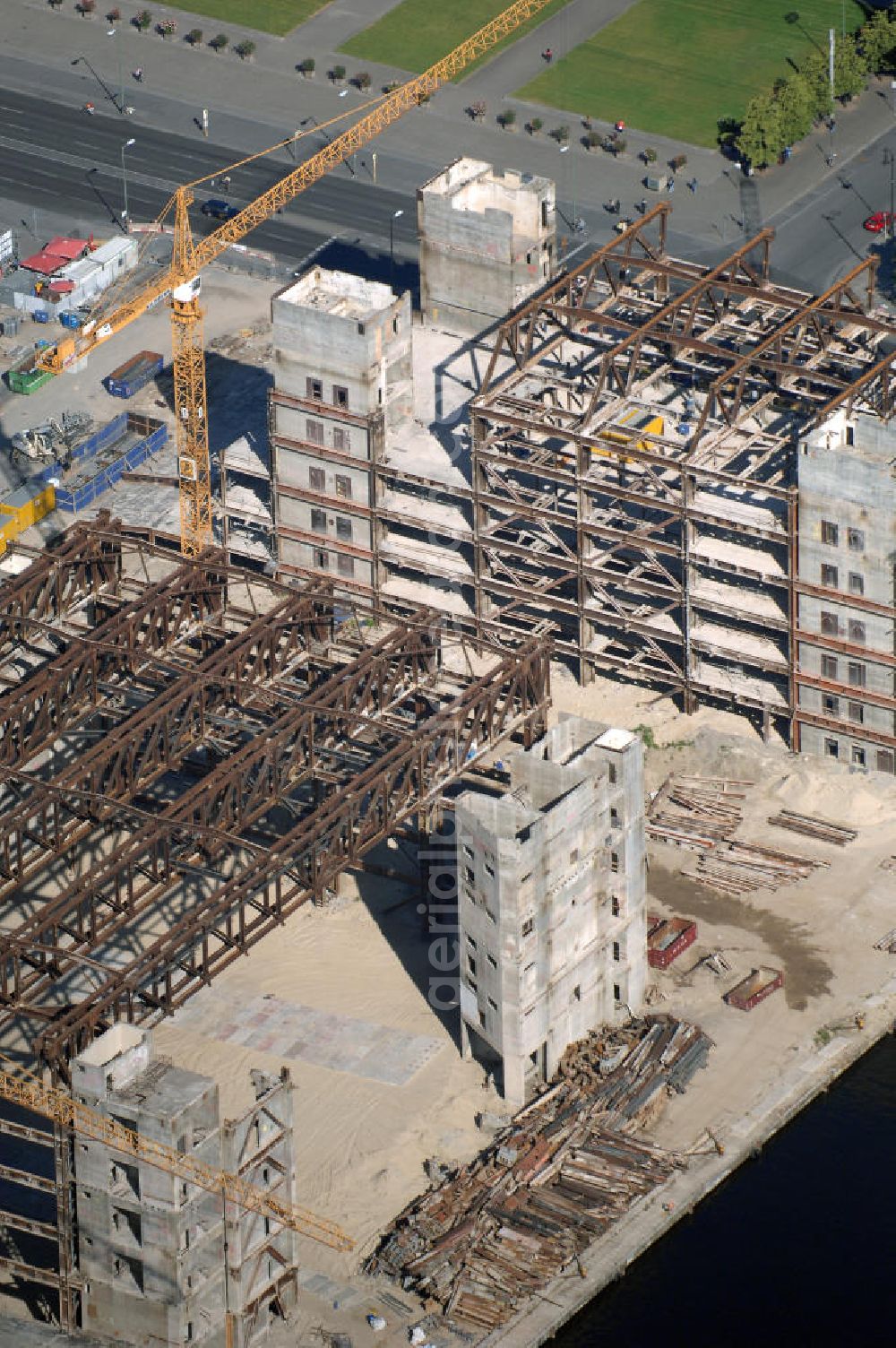 Aerial image Berlin - . Seit Februar 2006 wird der Palast langsam mit Hilfe von fünf Kränen abgerissen. Von einer Sprengung des Gebäudes wurde abgesehen, weil Beschädigungen umliegender Häuser durch den Auftrieb der Bodenwanne und das dadurch bedingte Absinken des Grundwasserspiegels befürchtet wurden. Stattdessen wird das abgetragene Material gemessen und dann im gleichen Maß mit Wasser versetzter Sand in die Bodenwanne geleitet. Die Abrissarbeiten sollten ursprünglich Mitte 2007 abgeschlossen sein. Nachdem im Laufe der Arbeiten an mehreren Stellen neuer Asbest gefunden wurde und sich der Abriss dadurch stark verlangsamte, wird mit Ende 2008 als frühestem Ende kalkuliert. Die Zusatzkosten in Höhe von bislang 9,9 Mio. Euro muss der Bund übernehmen. Nach der vollständigen Abtragung soll vorübergehend eine Grünfläche über der verbleibenden Bodenwanne entstehen.