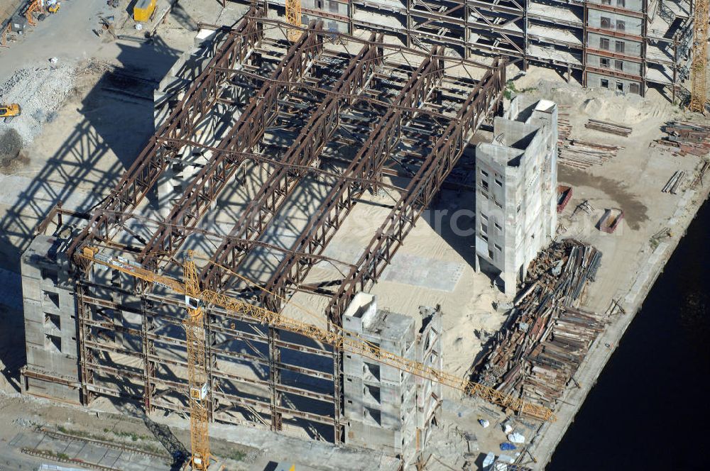 Berlin from above - . Seit Februar 2006 wird der Palast langsam mit Hilfe von fünf Kränen abgerissen. Von einer Sprengung des Gebäudes wurde abgesehen, weil Beschädigungen umliegender Häuser durch den Auftrieb der Bodenwanne und das dadurch bedingte Absinken des Grundwasserspiegels befürchtet wurden. Stattdessen wird das abgetragene Material gemessen und dann im gleichen Maß mit Wasser versetzter Sand in die Bodenwanne geleitet. Die Abrissarbeiten sollten ursprünglich Mitte 2007 abgeschlossen sein. Nachdem im Laufe der Arbeiten an mehreren Stellen neuer Asbest gefunden wurde und sich der Abriss dadurch stark verlangsamte, wird mit Ende 2008 als frühestem Ende kalkuliert. Die Zusatzkosten in Höhe von bislang 9,9 Mio. Euro muss der Bund übernehmen. Nach der vollständigen Abtragung soll vorübergehend eine Grünfläche über der verbleibenden Bodenwanne entstehen.