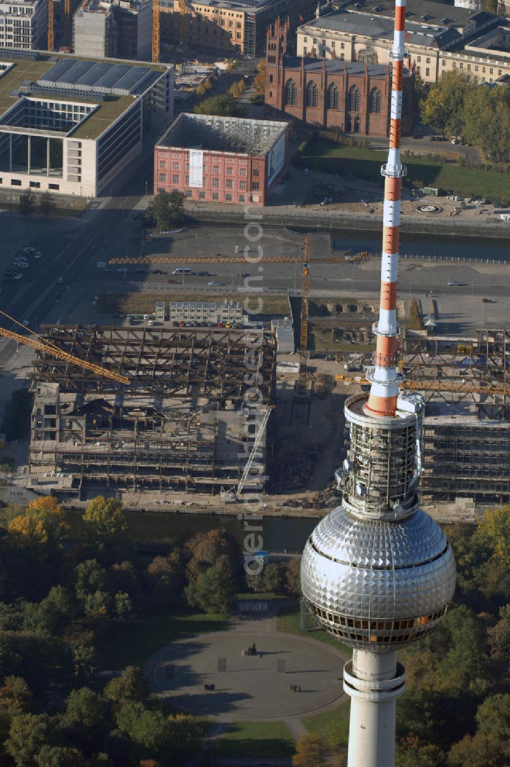 Aerial image Berlin - Blick auf den Abriss des Palast der Republik in Mitte.Der Rückbau des Palastes der Republik verschob sich immer wieder. Am 19. Januar 2006 beschloss der Deutsche Bundestag, Anträgen der Grünen und der Linkspartei zur Verschiebung des Abrisses bzw. zur Erhaltung des Bauwerks nicht stattzugeben.Nach Terminen im Frühjahr 2005 und im Oktober 2005 wird das Gebäude seit Februar 2006 langsam mithilfe von fünf Kränen zurückgebaut. Von einer Sprengung des Gebäudes wurde abgesehen, weil Beschädigungen umliegender Gebäude durch den Auftrieb der Bodenwanne und das dadurch bedingte Absinken des Grundwasserspiegels befürchtet wurden. Stattdessen wird das abgetragene Material gemessen und im gleichen Maß dann mit Wasser versetzter Sand in die Bodenwanne geleitet. Die Abrissarbeiten sollten ursprünglich Mitte 2007 abgeschlossen sein. Nachdem im Laufe der Arbeiten an mehreren Stellen neues Asbest gefunden wurde und sich der Abriss dadurch stark verlangsamte, wird mit Ende 2008 als frühestes Ende kalkuliert. Die Zusatzkosten in Höhe von bislang 9,9 Mio. Euro muss der Bund übernehmen.Nach der vollständigen Abtragung soll vorübergehend eine Grünfläche über der verbleibenden Bodenwanne entstehen. Diskutiert wird auch eine Zwischennutzung der Fläche durch eine Kunsthalle.