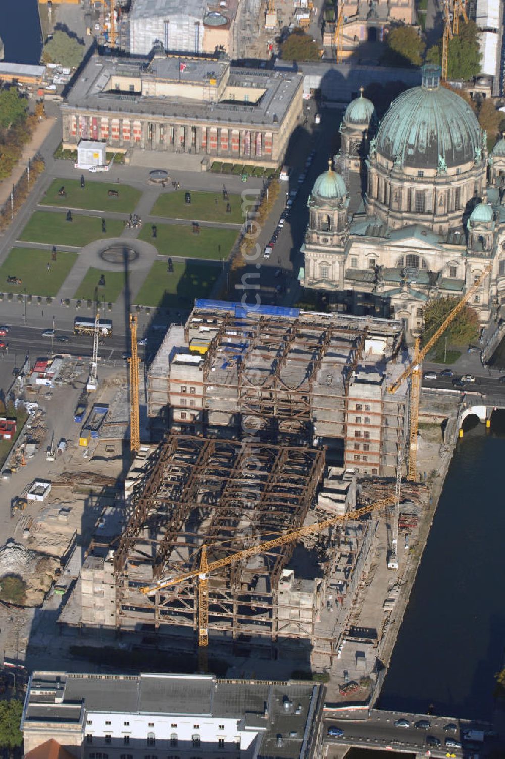 Aerial image Berlin - Blick auf den Abriss des Palast der Republik in Mitte.Der Rückbau des Palastes der Republik verschob sich immer wieder. Am 19. Januar 2006 beschloss der Deutsche Bundestag, Anträgen der Grünen und der Linkspartei zur Verschiebung des Abrisses bzw. zur Erhaltung des Bauwerks nicht stattzugeben.Nach Terminen im Frühjahr 2005 und im Oktober 2005 wird das Gebäude seit Februar 2006 langsam mithilfe von fünf Kränen zurückgebaut. Von einer Sprengung des Gebäudes wurde abgesehen, weil Beschädigungen umliegender Gebäude durch den Auftrieb der Bodenwanne und das dadurch bedingte Absinken des Grundwasserspiegels befürchtet wurden. Stattdessen wird das abgetragene Material gemessen und im gleichen Maß dann mit Wasser versetzter Sand in die Bodenwanne geleitet. Die Abrissarbeiten sollten ursprünglich Mitte 2007 abgeschlossen sein. Nachdem im Laufe der Arbeiten an mehreren Stellen neues Asbest gefunden wurde und sich der Abriss dadurch stark verlangsamte, wird mit Ende 2008 als frühestes Ende kalkuliert. Die Zusatzkosten in Höhe von bislang 9,9 Mio. Euro muss der Bund übernehmen.Nach der vollständigen Abtragung soll vorübergehend eine Grünfläche über der verbleibenden Bodenwanne entstehen. Diskutiert wird auch eine Zwischennutzung der Fläche durch eine Kunsthalle.