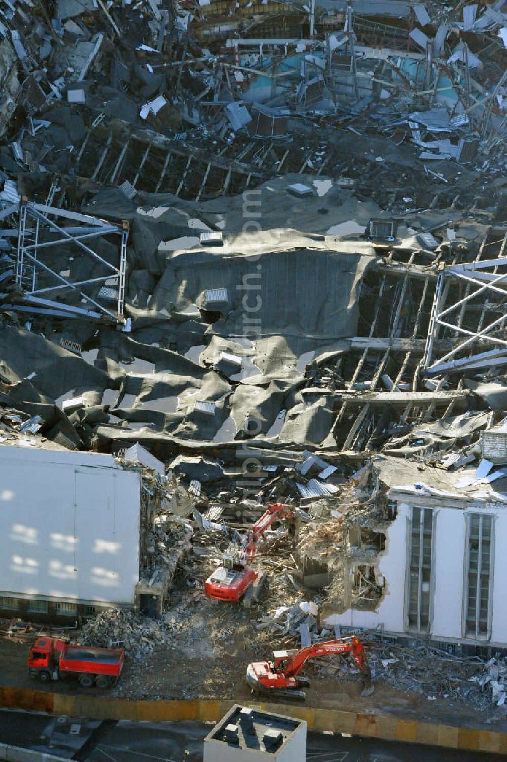 Aerial image Berlin - Blick auf die Abrißarbeiten an der ehemaligen Deutschlandhalle an der Jaffeystraße auf dem Messegelände in Charlottenburg. Abbruch-Bagger der Berliner Firma „ RWG1 “ setzten sie ihre tonnenschweren Kneifzangen in Betrieb und hackten sich in den Beton. Begonnen wurde mit dem Fassaden-Abriss an der Nordseite der Halle mit Abbruch-Bagger der Marke „ Liebherr “, Modelle 954 und 974. Sie wiegen 87 bis 140 Tonnen, haben bis zu 543 PS, nehmen die Fassade mit verschiedenen Greif- und Kneifbacken in die Zange. Der Abbruch soll bis März des Folgejahres beendet sein, um die nötige Baufreiheit für die Grundsteinlegung einer neuen Kongress- und Messehalle der Messe Berlin zu gewährleisten. Demolition work of the former Germany Halle Jaffeystraße on the fairgrounds in Charlottenburg.