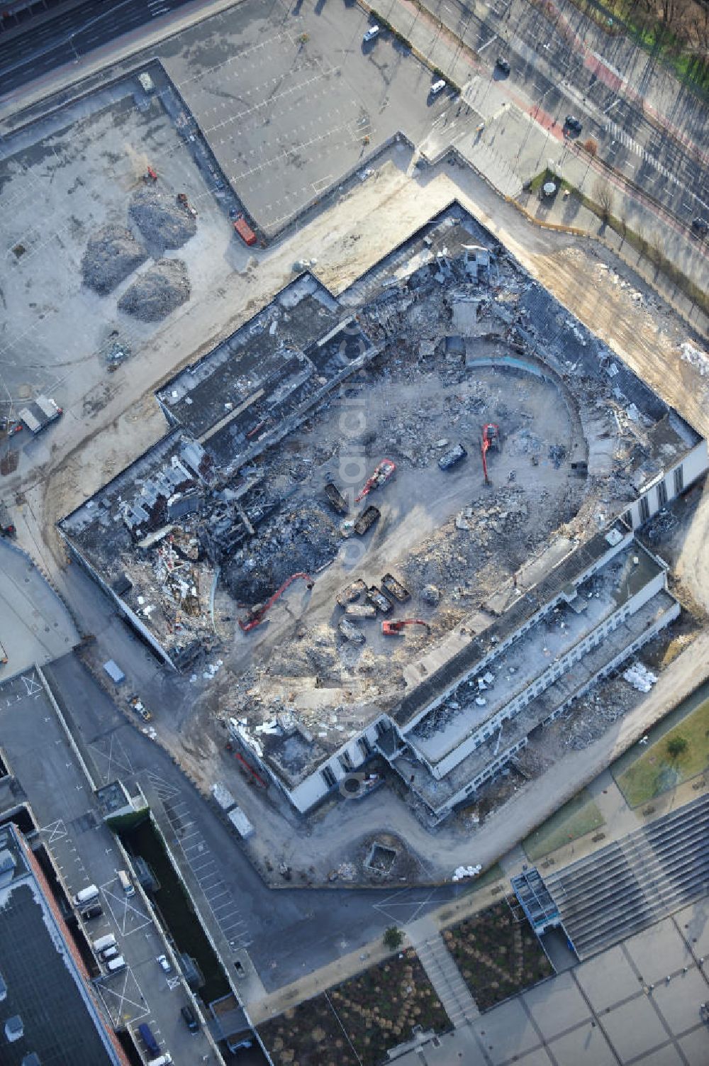 Aerial photograph Berlin - Blick auf die Abrißarbeiten an der ehemaligen Deutschlandhalle an der Jaffeystraße auf dem Messegelände in Charlottenburg. Abbruch-Bagger der Berliner Firma „ RWG1 “ setzten sie ihre tonnenschweren Kneifzangen in Betrieb und hackten sich in den Beton. Begonnen wurde mit dem Fassaden-Abriss an der Nordseite der Halle mit Abbruch-Bagger der Marke „ Liebherr “, Modelle 954 und 974. Sie wiegen 87 bis 140 Tonnen, haben bis zu 543 PS, nehmen die Fassade mit verschiedenen Greif- und Kneifbacken in die Zange. Der Abbruch soll bis März des Folgejahres beendet sein, um die nötige Baufreiheit für die Grundsteinlegung einer neuen Kongress- und Messehalle der Messe Berlin zu gewährleisten. Demolition work of the former Germany Halle Jaffeystraße on the fairgrounds in Charlottenburg.