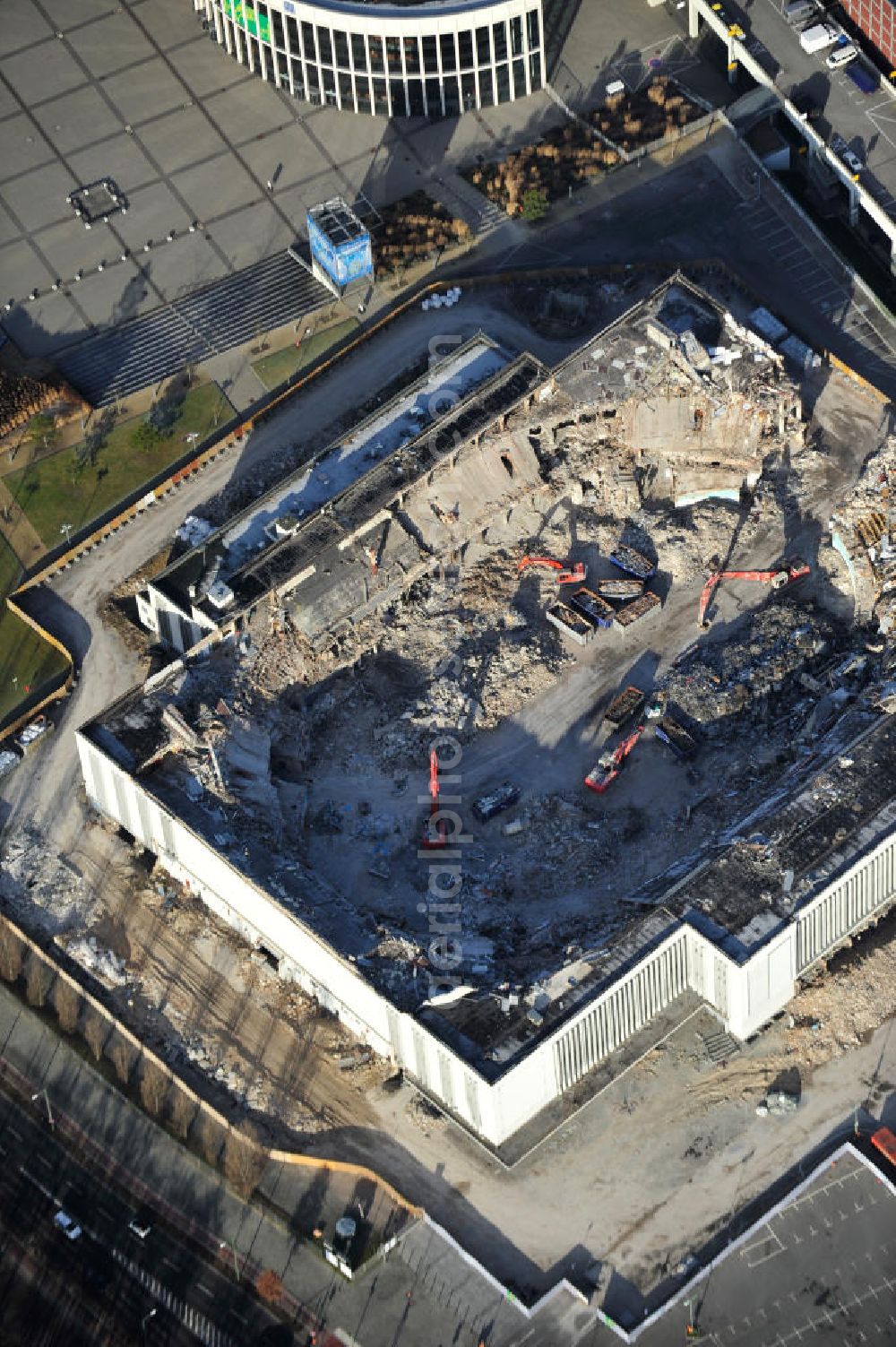 Aerial photograph Berlin - Blick auf die Abrißarbeiten an der ehemaligen Deutschlandhalle an der Jaffeystraße auf dem Messegelände in Charlottenburg. Abbruch-Bagger der Berliner Firma „ RWG1 “ setzten sie ihre tonnenschweren Kneifzangen in Betrieb und hackten sich in den Beton. Begonnen wurde mit dem Fassaden-Abriss an der Nordseite der Halle mit Abbruch-Bagger der Marke „ Liebherr “, Modelle 954 und 974. Sie wiegen 87 bis 140 Tonnen, haben bis zu 543 PS, nehmen die Fassade mit verschiedenen Greif- und Kneifbacken in die Zange. Der Abbruch soll bis März des Folgejahres beendet sein, um die nötige Baufreiheit für die Grundsteinlegung einer neuen Kongress- und Messehalle der Messe Berlin zu gewährleisten. Demolition work of the former Germany Halle Jaffeystraße on the fairgrounds in Charlottenburg.