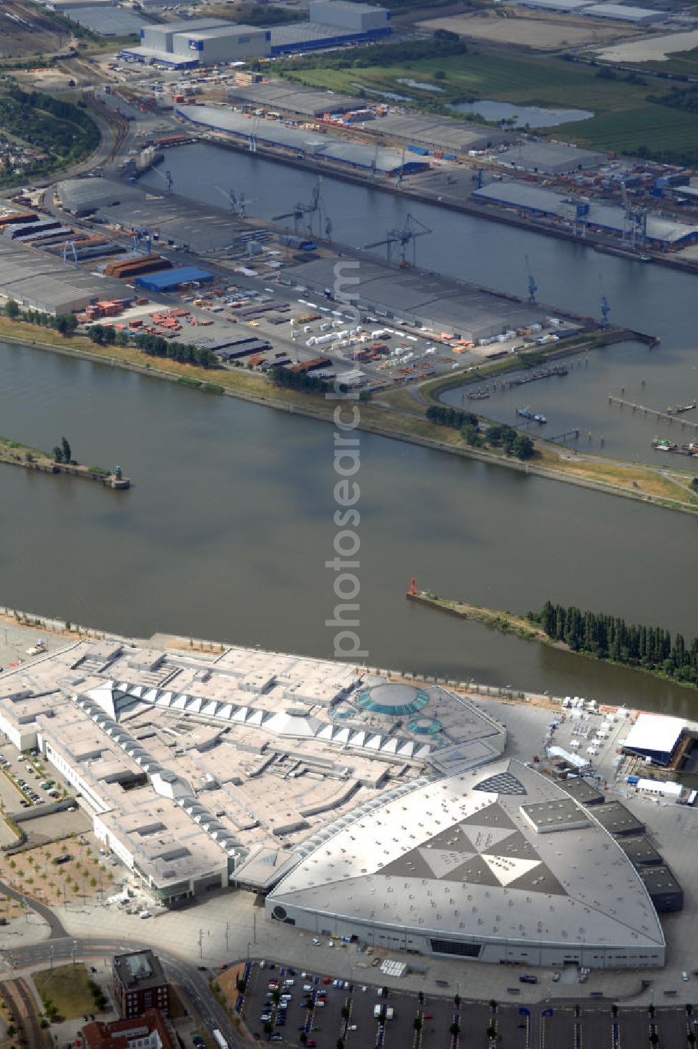 BREMEN from the bird's eye view: Areal des Space Parks Bremen. Das Projekt wurde Anfang der 1990er Jahre von der in Wiesbaden ansässigen, inzwischen nicht mehr existenten Köllmann AG zusammen mit dem noch nicht realisierten Ocean Park in Bremerhaven geplant. Der Kerngedanke ist dabei die für Urban Entertainment Center typische Verbindung von Unterhaltung und Einzelhandel. Das Projekt wurde mit Unterstützung des Landes Bremen in Form von Subventionen unter Bauherrenschaft der zur Dresdner Bank gehörenden DEGI realisiert. Der Bau wurde im Juli 2000 begonnen und war am 19. Dezember 2003 fertig gestellt. Eröffnet wurde der Park am 12. Februar 2004.Der Space Park wurde an die britische Finanzinvestorengruppe „Cardinal Asset Management“ verkauft. Diese erklärte von Beginn an, den Space Park nicht selbst betreiben zu wollen, und verkaufte ihn schließlich für 50 Millionen Euro an den irischen Finanzdienstleister LNC Property Group. Im Februar 2007 kündigte der LNC-Chef Bill McCabe an, dass die LNC weitere 80 bis 100 Millionen Euro investieren wolle, um das Areal baulich zur Weser hin auszurichten und den Einzelhandelsbereich des Space Parks unter dem Namen „Waterfront Bremen“ im September 2008 wiederzueröffnen. Bis 2009 soll ein Sport-, Freizeit- und Wellnessbereich hinzukommen. Kalkuliert ist ein Einzugsgebiet mit einem Durchmesser von 200 Kilometern und eine Besucherzahl von im Durchschnitt täglich 25.000 Besuchern. Im Frühjahr 2007 wurde das Space Park Logo entfernt. Seit Anfang August hängt der Name Waterfront am Eingang. Limetree GmbH, AG-Weser-Straße 3 , 28237 Bremen,Telefon: +49 4213305 300;