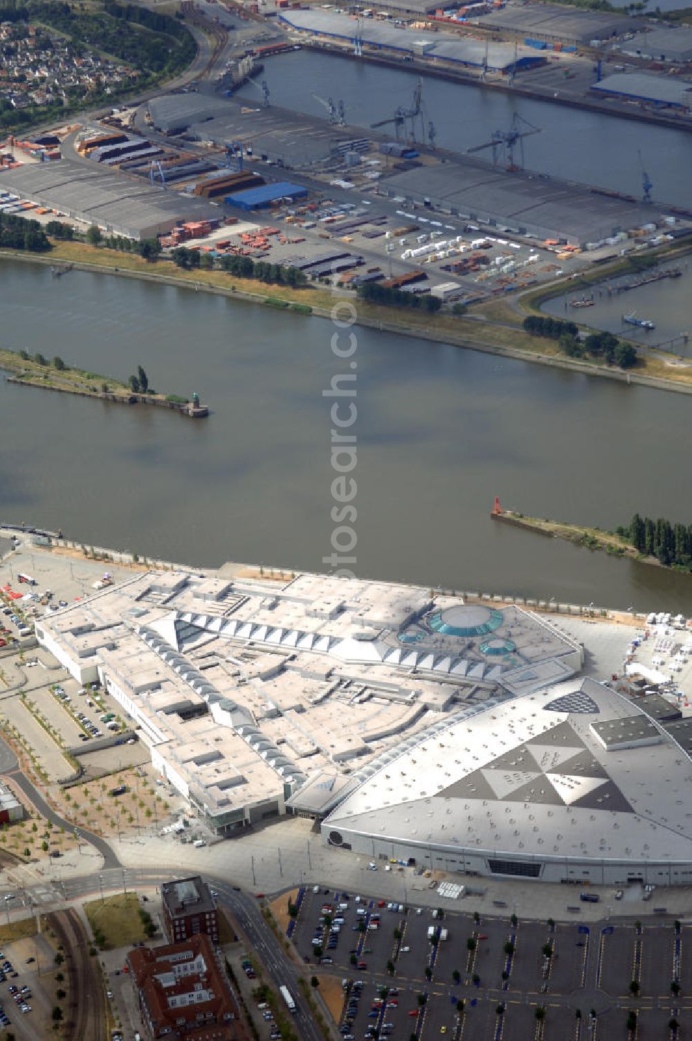 Aerial photograph BREMEN - Areal des Space Parks Bremen. Das Projekt wurde Anfang der 1990er Jahre von der in Wiesbaden ansässigen, inzwischen nicht mehr existenten Köllmann AG zusammen mit dem noch nicht realisierten Ocean Park in Bremerhaven geplant. Der Kerngedanke ist dabei die für Urban Entertainment Center typische Verbindung von Unterhaltung und Einzelhandel. Das Projekt wurde mit Unterstützung des Landes Bremen in Form von Subventionen unter Bauherrenschaft der zur Dresdner Bank gehörenden DEGI realisiert. Der Bau wurde im Juli 2000 begonnen und war am 19. Dezember 2003 fertig gestellt. Eröffnet wurde der Park am 12. Februar 2004.Der Space Park wurde an die britische Finanzinvestorengruppe „Cardinal Asset Management“ verkauft. Diese erklärte von Beginn an, den Space Park nicht selbst betreiben zu wollen, und verkaufte ihn schließlich für 50 Millionen Euro an den irischen Finanzdienstleister LNC Property Group. Im Februar 2007 kündigte der LNC-Chef Bill McCabe an, dass die LNC weitere 80 bis 100 Millionen Euro investieren wolle, um das Areal baulich zur Weser hin auszurichten und den Einzelhandelsbereich des Space Parks unter dem Namen „Waterfront Bremen“ im September 2008 wiederzueröffnen. Bis 2009 soll ein Sport-, Freizeit- und Wellnessbereich hinzukommen. Kalkuliert ist ein Einzugsgebiet mit einem Durchmesser von 200 Kilometern und eine Besucherzahl von im Durchschnitt täglich 25.000 Besuchern. Im Frühjahr 2007 wurde das Space Park Logo entfernt. Seit Anfang August hängt der Name Waterfront am Eingang. Limetree GmbH, AG-Weser-Straße 3 , 28237 Bremen,Telefon: +49 4213305 300;