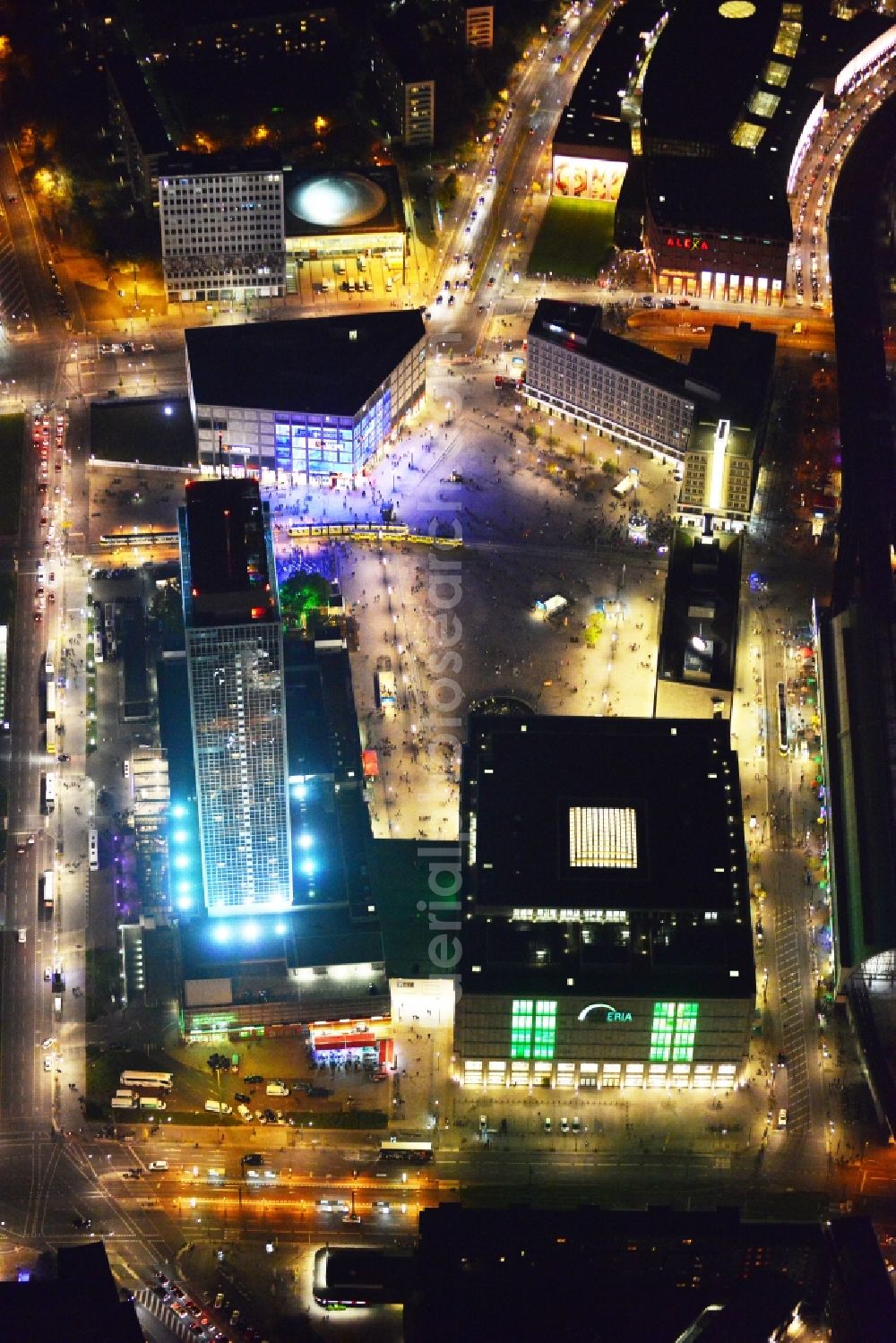 Berlin at night from the bird perspective: Night aerial view overlooking illuminated buildings at Alexanderplatz in the city center of Berlin. Visible among others are the department stores Saturn and Galeria Kaufhof as well as the Park Inn Hotel