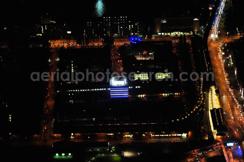 Aerial image at night Berlin - Nachtaufnahme: Oberbaum-City, das Gelände der ehemaligen Narva Lampenfabrik, in Berlin-Friedrichshain zwischen U-Bahnhof und S-Bahnhof Warschauer Straße. Das markanteste Bauwerk ist der Narva-Turm, das erste Hochhaus von Berlin, daneben die U-Bahn-Abstellanlage entlang der Rudolfstraße. Night Shot: Oberbaum City in Berlin-Friedrichshain with the Narva-Tower, the first tower building of Berlin. Next to it the storage siding of Berlin subway along the street Rudolfstrasse.