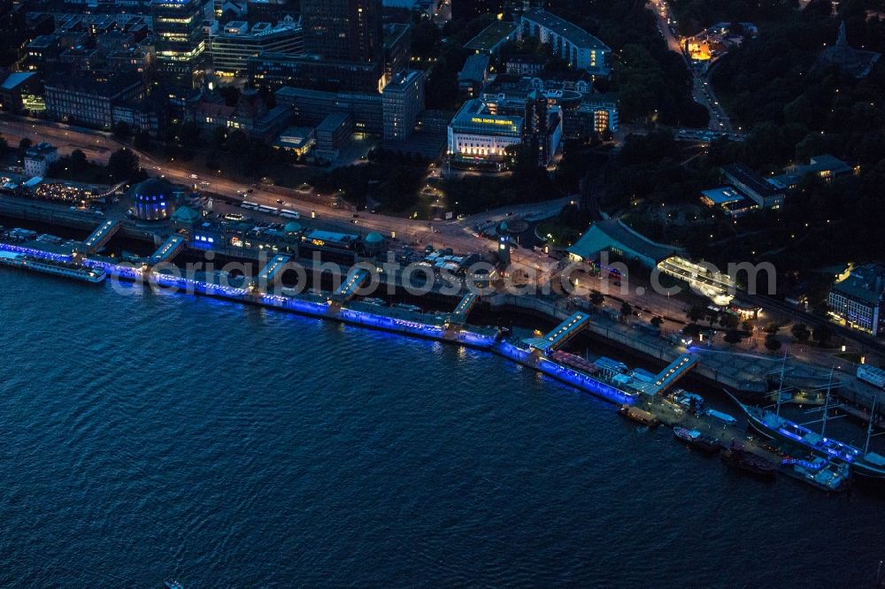 Hamburg at night from above - Night aerial view of the Landungsbrücken on the banks of the Elbe in Hamburg's St. Pauli district. The Landungsbrücken are forming a central hub of S-Bahn, U-Bahn and boat travel. The pier terminal building is a tourist attraction and listed as a landmark since 2003. Also visible is the Hotel Hafen Hamburg and the Federal Maritime and Hydrographic Agency