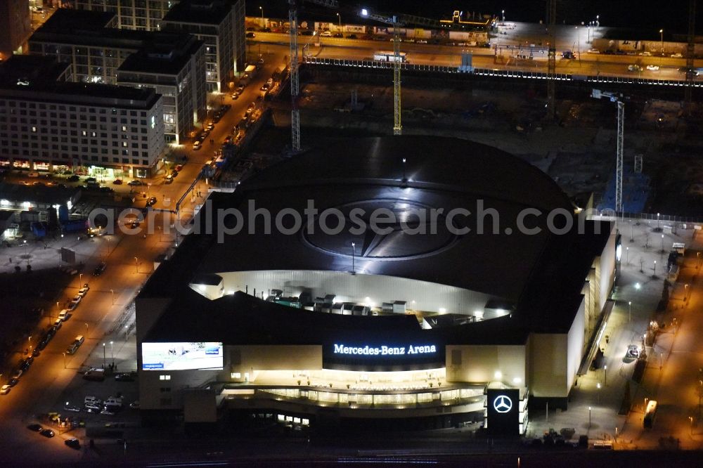 Aerial image at night Berlin - Night view of Mercedes-Benz-Arena on the Spree riverbank in the Friedrichshain part of Berlin. The former O2 World - now Mercedes-Benz-Arena - is located in the Anschutz Areal, a business and office space on the riverbank