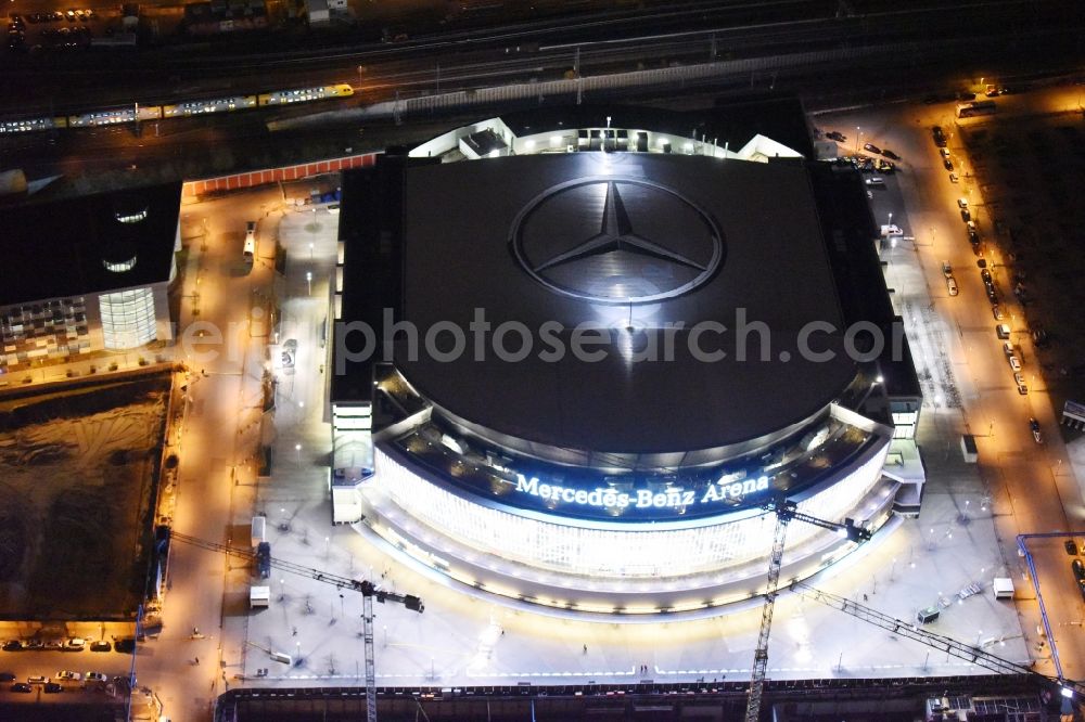 Aerial photograph at night Berlin - Night view of Mercedes-Benz-Arena on the Spree riverbank in the Friedrichshain part of Berlin. The former O2 World - now Mercedes-Benz-Arena - is located in the Anschutz Areal, a business and office space on the riverbank