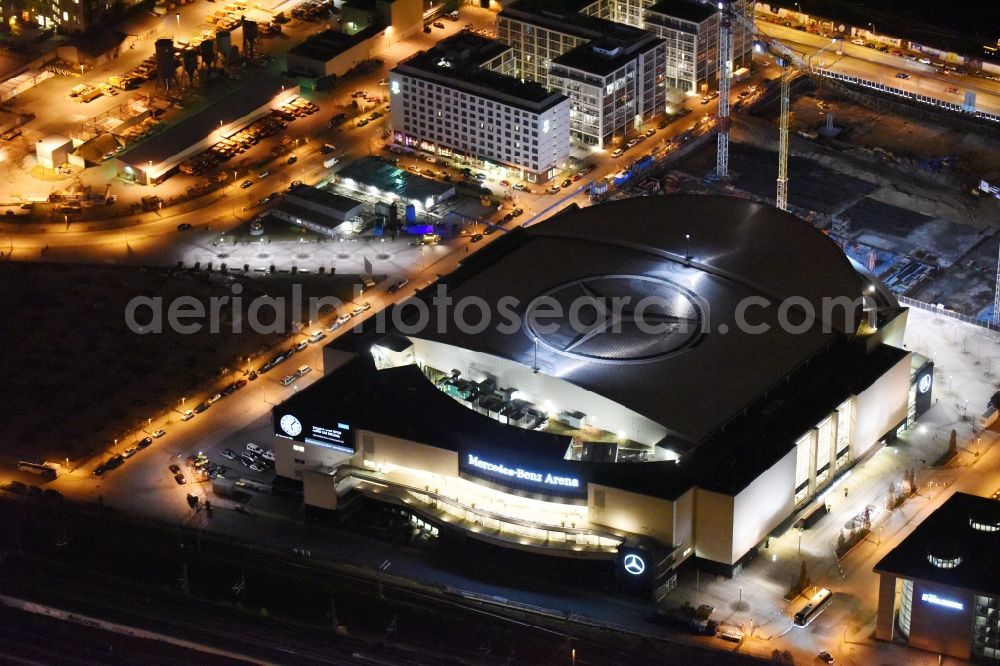 Aerial image at night Berlin - Night view of Mercedes-Benz-Arena on the Spree riverbank in the Friedrichshain part of Berlin. The former O2 World - now Mercedes-Benz-Arena - is located in the Anschutz Areal, a business and office space on the riverbank