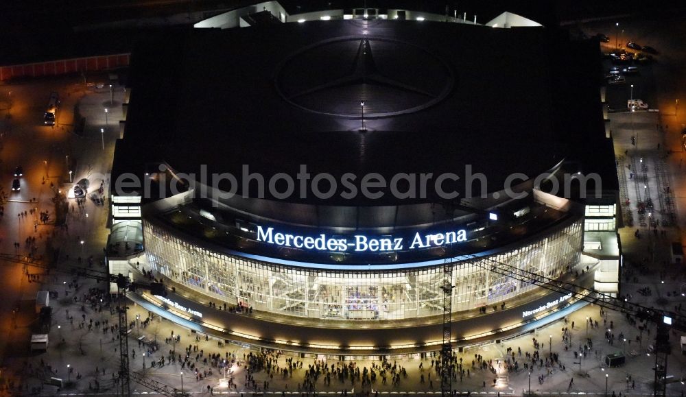 Aerial image at night Berlin - Night view of Mercedes-Benz-Arena on the Spree riverbank in the Friedrichshain part of Berlin. The former O2 World - now Mercedes-Benz-Arena - is located in the Anschutz Areal, a business and office space on the riverbank