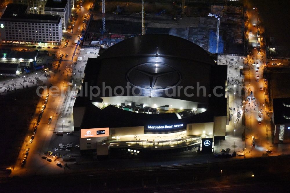 Aerial photograph at night Berlin - Night view of Mercedes-Benz-Arena on the Spree riverbank in the Friedrichshain part of Berlin. The former O2 World - now Mercedes-Benz-Arena - is located in the Anschutz Areal, a business and office space on the riverbank