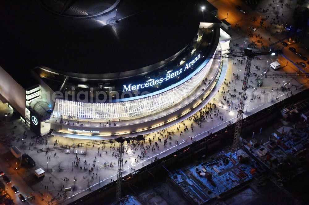 Aerial photograph at night Berlin - Night view of Mercedes-Benz-Arena on the Spree riverbank in the Friedrichshain part of Berlin. The former O2 World - now Mercedes-Benz-Arena - is located in the Anschutz Areal, a business and office space on the riverbank