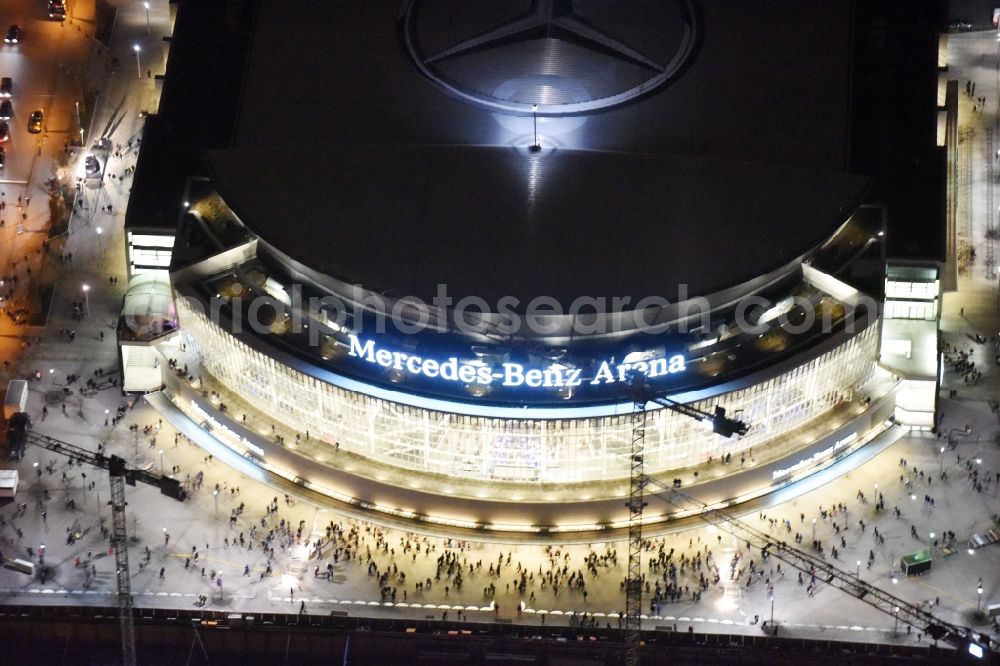 Aerial photograph at night Berlin - Night view of Mercedes-Benz-Arena on the Spree riverbank in the Friedrichshain part of Berlin. The former O2 World - now Mercedes-Benz-Arena - is located in the Anschutz Areal, a business and office space on the riverbank