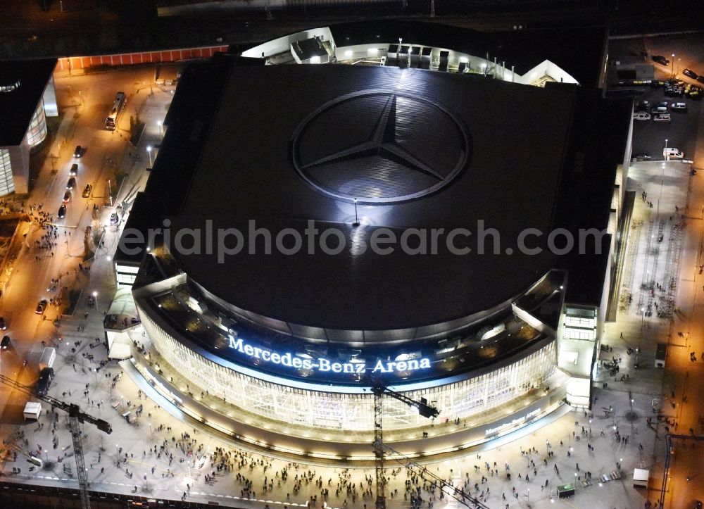 Aerial image at night Berlin - Night view of Mercedes-Benz-Arena on the Spree riverbank in the Friedrichshain part of Berlin. The former O2 World - now Mercedes-Benz-Arena - is located in the Anschutz Areal, a business and office space on the riverbank