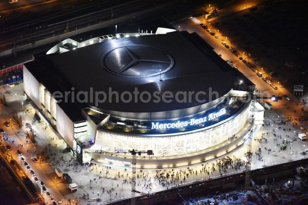 Aerial photograph at night Berlin - Night view of Mercedes-Benz-Arena on the Spree riverbank in the Friedrichshain part of Berlin. The former O2 World - now Mercedes-Benz-Arena - is located in the Anschutz Areal, a business and office space on the riverbank