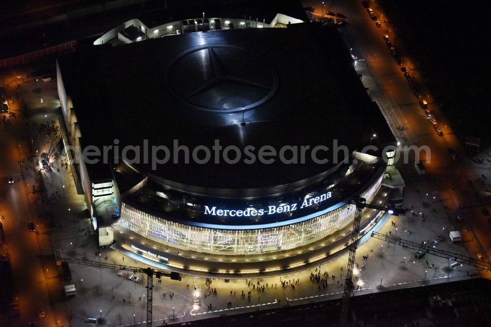 Aerial photograph at night Berlin - Night view of Mercedes-Benz-Arena on the Spree riverbank in the Friedrichshain part of Berlin. The former O2 World - now Mercedes-Benz-Arena - is located in the Anschutz Areal, a business and office space on the riverbank