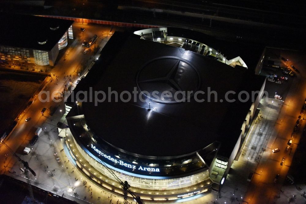 Aerial photograph at night Berlin - Night view of Mercedes-Benz-Arena on the Spree riverbank in the Friedrichshain part of Berlin. The former O2 World - now Mercedes-Benz-Arena - is located in the Anschutz Areal, a business and office space on the riverbank