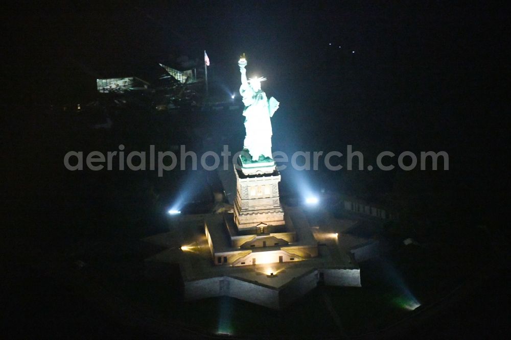 Aerial image at night New York - Night lighting Tourist attraction of the historic monument Freiheitsstatue - Statue of Liberty National Monument in the district Manhattan in New York in United States of America