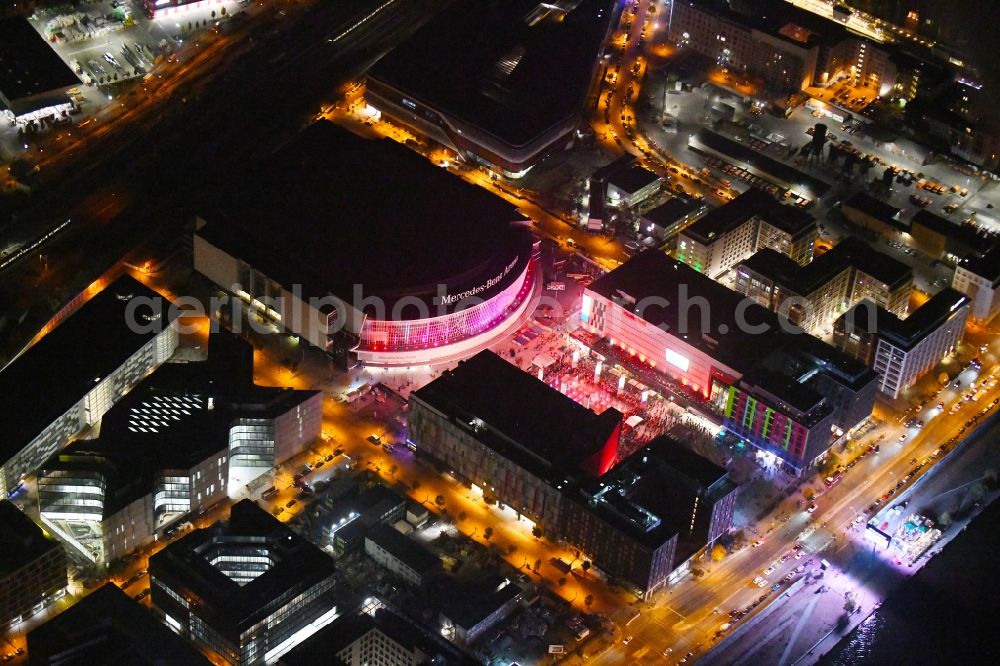 Aerial photograph at night Berlin - Night lighting Arena Mercedes-Benz-Arena on Friedrichshain part of Berlin. The former O2 World - now Mercedes-Benz-Arena - is located in the Anschutz Areal, a business and office space on the riverbank