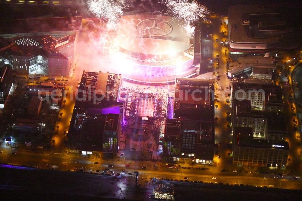 Aerial photograph at night Berlin - Night lighting Arena Mercedes-Benz-Arena on Friedrichshain part of Berlin. The former O2 World - now Mercedes-Benz-Arena - is located in the Anschutz Areal, a business and office space on the riverbank