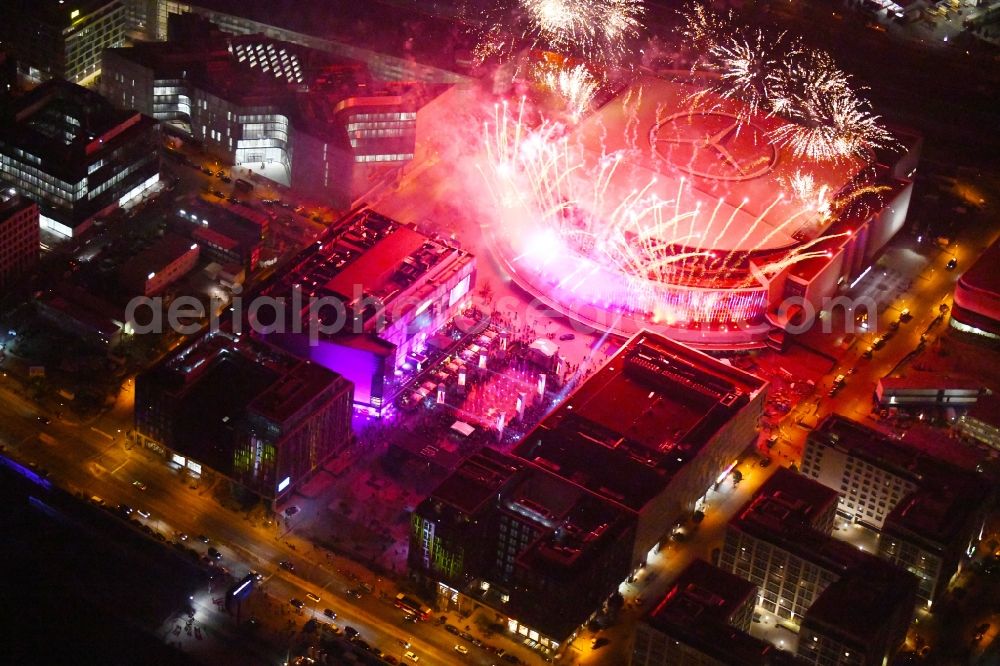 Aerial photograph at night Berlin - Night lighting Arena Mercedes-Benz-Arena on Friedrichshain part of Berlin. The former O2 World - now Mercedes-Benz-Arena - is located in the Anschutz Areal, a business and office space on the riverbank