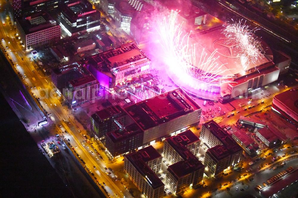 Aerial photograph at night Berlin - Night lighting Arena Mercedes-Benz-Arena on Friedrichshain part of Berlin. The former O2 World - now Mercedes-Benz-Arena - is located in the Anschutz Areal, a business and office space on the riverbank