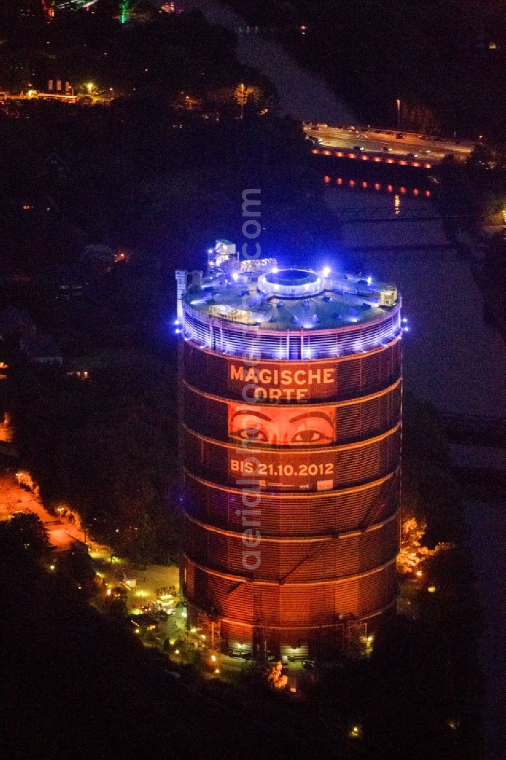 Oberhausen at night from above - Night-time air picture from the Gasometer Oberhausen in Action extra layer 2012th The gasometer is the symbol of the city of Oberhausen, impressive document the construction and history of technology and venue