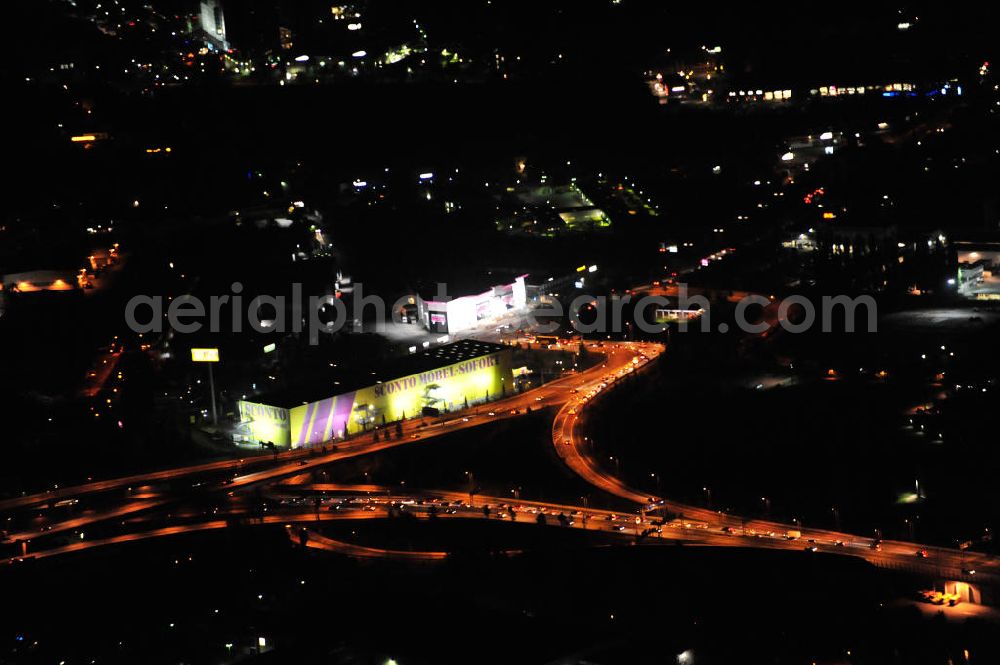 Berlin at night from the bird perspective: Nachtaufnahme: Filiale der Firma Sconto SB – Der Möbelmarkt GmbH in der Grenzallee in Berlin-Neukölln, dahinter die Filiale der Firma SB-MÖBEL BOSS Handelsgesellschaft mbH & Co. KG gegenüber der Autobahnausfahrt Grenzallee der A113 am Autobahndreieck Neukölln. Night shot: Stores of two furniture selling stores at the freeway exit Grenzallee at the motorway junction Neukoelln.