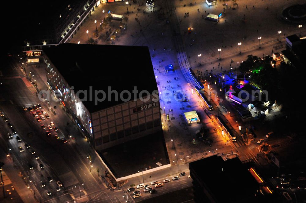 Berlin at night from the bird perspective: Nachtaufnahme: Blick auf den mit 10.000 Quadratmeter Verkaufsfläche größten Saturn-Markt Deutschlands mit blauer Beleuchtung. Das Elektronik-Unternehmen bezog das neue Geschäftshaus direkt auf dem Alexanderplatz nahe der Kreuzung Alexan derstraße / Karl-Marx-Allee. Night Shot: View to the illuminated Saturn electrical market at the square Alexanderplatz.