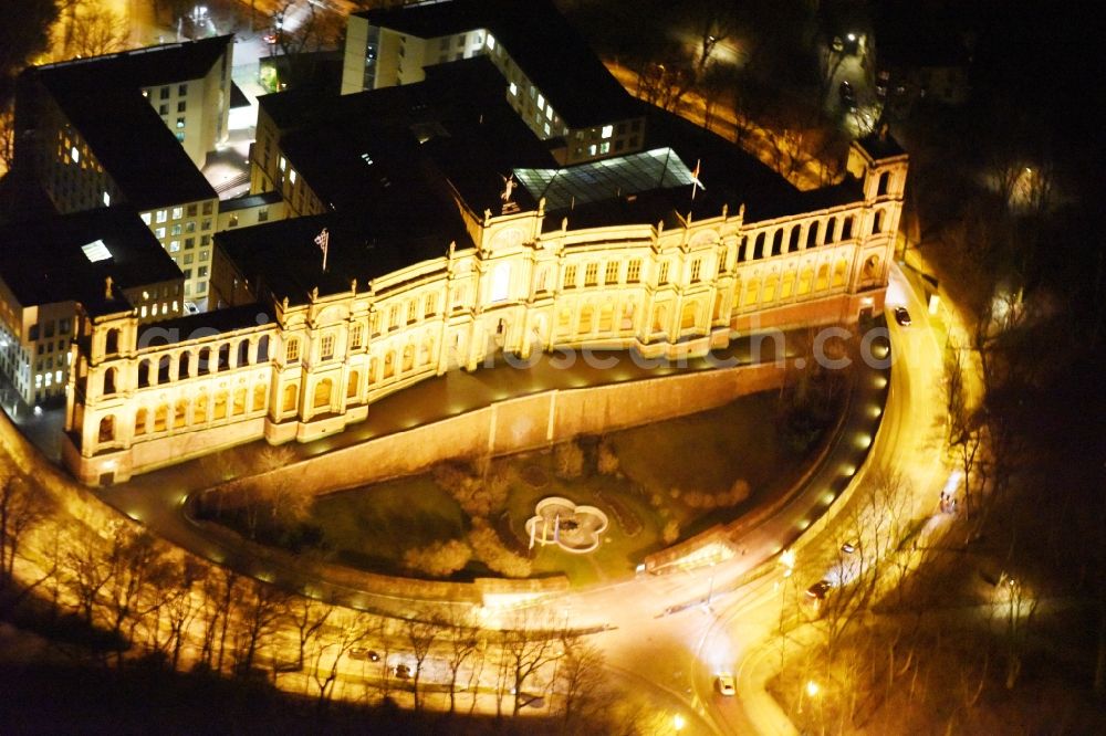 München at night from the bird perspective: Night view of palatial building Maximilianeum in the Haidhausen part of Munich in the state of Bavaria. The historic building is located on the Maximilian Bridge and includes the foundation Maximilianeum and has been seat of the Bavarian parliament. Because of its distinct facade and adjacent park with fountain, it is one of the famous tourist sites of the city