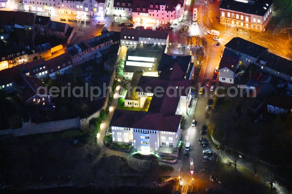 Strausberg at night from the bird perspective: Night lighting Banking administration building of the financial services company Sparkasse on Karl-Liebknecht-Strasse coner Grosse Strasse in Strausberg in the state Brandenburg, Germany