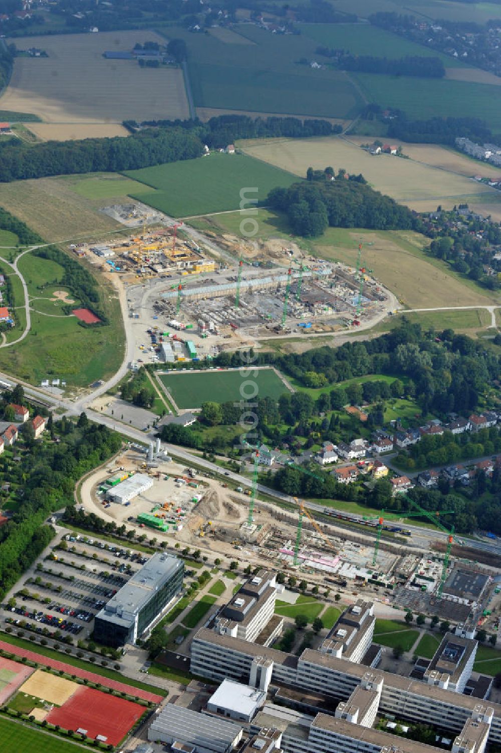 Aerial photograph Bielefeld - Die Universität Bielefeld wird ausgebaut. Es entstehen drei neue Gebäude. Auf dem ehemaligen Parkplatz der Uni, unten im Bild zu sehen, entsteht der Ersatzneubau Universitätsstraße, kurz ENUS. Nach der Fertigstellung wird die Mensa dort unterkommen. Nördlich davon entsteht eine Fachhochschule sowie ein weiteres Forschungsgebäude. Bauherr ist die BAM Deutschland AG. The Bielefeld University is going to be enlarged. 3 new buildings will be raised. The former parking area will be turned into a building called ENUS. After finishing the building it will be the home of the canteen. The northern construction site is building a college and a research centre.