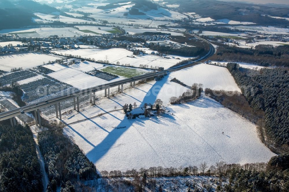 Aerial photograph Meschede - Winterly snowy routing and traffic lanes over the highway bridge Talbruecke Wennemen in the motorway A 46 and its surrounding fields and forestland in Meschede in the state North Rhine-Westphalia