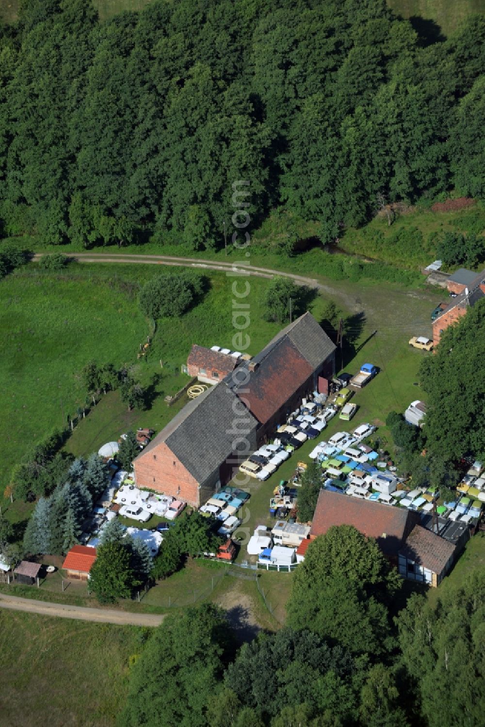 Gräfenhainichen from the bird's eye view: Farm in the North of the Tornau part of the town of Graefenhainichen in the state of Saxony-Anhalt. The agricultural estate is located at a forest and surrounded by meadows. Several cars of the Trabant brand or Trabi are located on the compound