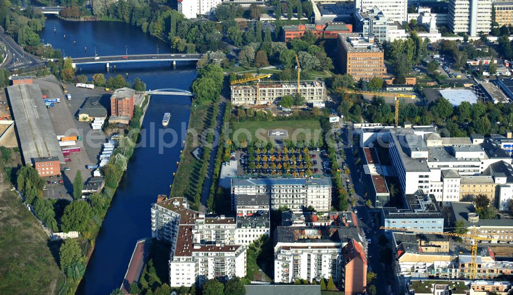 Aerial photograph Berlin - Blick über Mehrfamilienhäuser auf die Baustelle der Wohnanlage Hafenquartier Mitte, das Bundeswehrkrankenhaus mit Hubschrauberlandeplatz, das Umspannwerk Scharnhorst, den Nordhafen mit Nordhafenbrücke und die Kieler Brücke in Berlin-Mitte am Spreeufer. View over the construction site of the apartment complex Hafenquartier Mitte, the Bundeswehr hospital with helipad, the transformer station Scharnhorst, the part of the Spree Nordhafen with the bridge Nordhafen and the bridge Kieler Brücke in Berlin-Mitte at the riverside of the Spree.