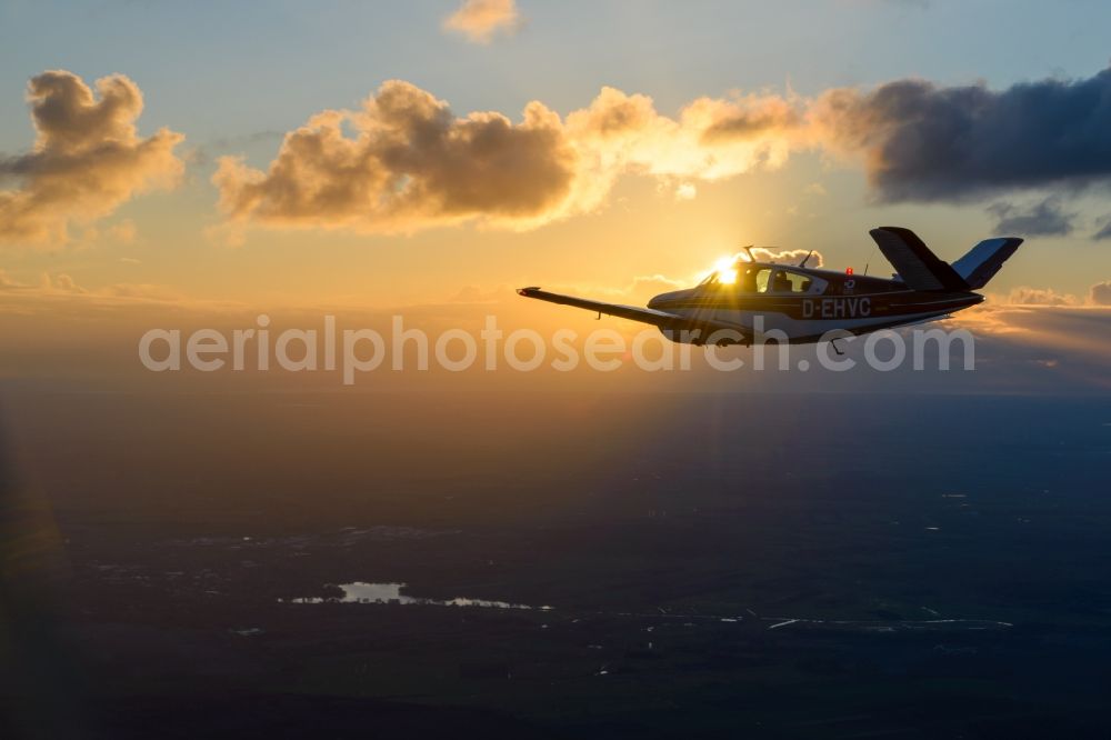 Geestland from the bird's eye view: Beechcraft Bonanza D-EHVC in flight while sunet near Geestland in the state of Bremen, Germany. The Beechcraft Bonanza is produced by Beech Aircraft Corporation as a travel and business aircraft