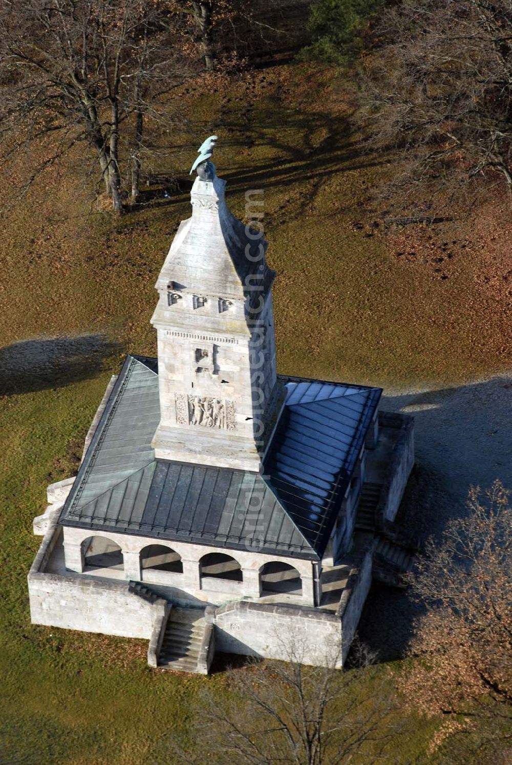 Assenhausen from above - Blick auf den Bismarckturm in Assenhausen am Starnberger See. Im Jahre 1890 wurde in München unter dem Vorsitz des Malers Prof. Dr. Franz von Lenbach und Bürgermeister Dr. von Widenmayer ein Komitee zur Errichtung einer Bismarcksäule gegründet. Die Einweihung des 30 m hohen Ehrenturmes fand am 01.07.1899 statt. Der Bismarck-Verein schenkte das Denkmal (mit 9,172 Hektar großem Grundstück) der Stadt München. Um den quadratischen Sockel des Turmes läuft eine mit 16 offenen Rundbögen gebildete Wandelhalle. Von allen vier Seiten führen Treppen zur Wandelhalle. In der Halle sind Wappenschilde der Bundesstaaten und freien Städte, an der Nordseite eine Bismarck-Widmungstafel mit den Portraitköpfen Karls des Großen, Friedrich Barbarossas, Ottos des Großen, Goethes, Dürers und Beethovens (Vorbilder Bismarcks) angebracht. Der Turm ist bekrönt von einem kupfernen Adler (hergestellt von Kiehne). Als Material für den Turm wurden Kalkstein und Tuff verwendet. Die künstlerische Gestaltung (außen und innen) oblag den Bildhauern H. Flossmann und Georg Wrba. Die Bronzetafel mit Bismarckwappen und Reichsadlerrelief (s. Foto oben mitte) wurde von der Erzgießerei Renaissance (Johann Lampel) hergestellt.