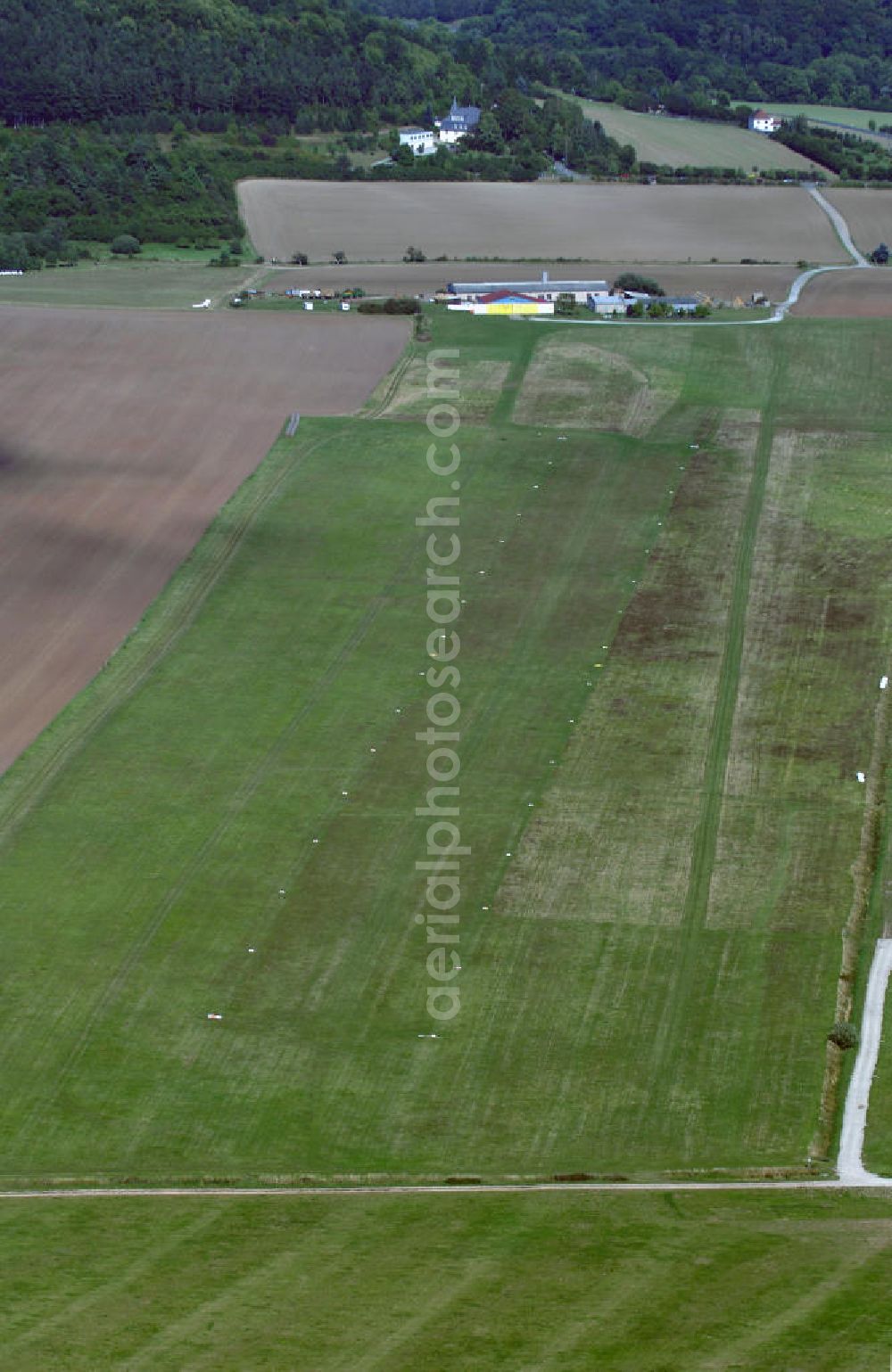 Aerial image Bad Berka - Blick auf den Flugplatz Bad Berka. Im Jahr 1962 wurde er eröffnet und von Luftsportlern aus Bad Berka, Weimar und der Umgebung genutzt. Auf Grund zu hoher Kosten wurde der Platz 1979 geschlossen, jedoch nach der Wiedervereinigung 1990 erneut geöffnet. Seitdem ist er bei Segelfliegern aus ganz Deutschland und dem Ausland sehr beliebt. Zum Platz gehören auch eine Flughalle, die 1999 neu gebaut wurde mit dazugehörigem Clubraum und einem Campingplatz. Genutzt wird der Flugplatz vor allem von dem Fliegerclub Bad Berka - Weimar e.V. Kontakt: Fliegerclub Bad Berka - Weimar e.V., Am Hexenberg 99438 Bad Berka, Tel. +49(0)36458 41173, Fax +49(0)361 3451904, Email: info@fcbb.de