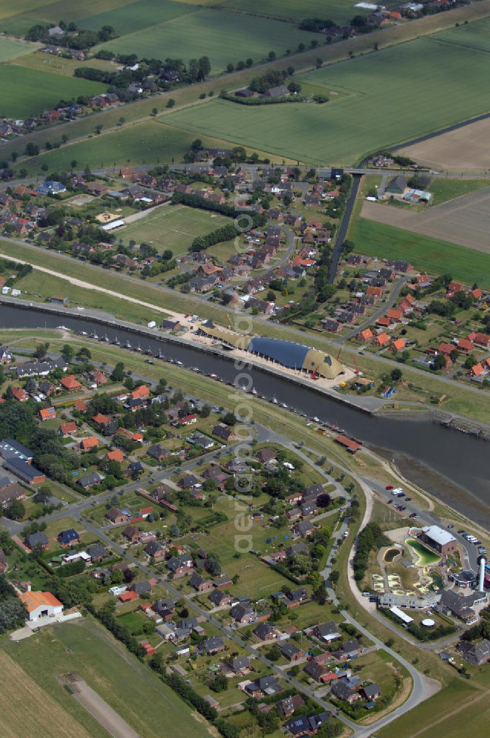 Aerial image Friedrichskoog - Blick auf Friedrichskoog mit Hafen und Baustelle. Friedrichskoog ist eine Gemeinde im Südwesten des Kreis Dithmarschen zwischen der offenen Nordsee und der Elbmündung. Ursprünglich durch Landwirtschaft geprägt kam Anfang des 20. Jahrhunderts die Fischerei hinzu, mittlerweile ist es vor allem ein Touristenort. Die Stadt hat ca. 2400 Einwohner und ist bekannt für ihre Seehundstation. Der Friedrichskooger Hafen wurde 1853-1854 gebaut. Damals wie heute dient er vor allem als Hafen für Fisch und Krabben. In der Nähe entsteht zur Zeit eine Indoorspielhalle in Form eines Wal. Kontakt: Tourismus-Service Friedrichskoog, Koogstraße 141, 25718 Friedrichskoog, Tel. +49 (0)4854 90494 0, Fax +49 (0)4854 90494 19, EMail info@friedrichskoog.de