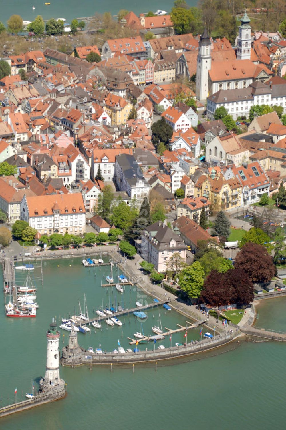 Lindau from above - Blick auf die Lindau Insel mit Hafen, Mangturm und Altstadt. Die Hafeneinfahrt an der Lindau Insel ist von einem Leuchtturm und dem Bayerischen Löwen begrenzt. Der Mangturm wurde um 1200 als Leuchtturm erbaut und war der Turm der ehemaligen Stadtbefestigung. Als besonderer Hingucker dient hier das bunte Dach, welches aus dem 19. Jhd. stammt. Seinen Namen hat er durch das ehemalige Tuch- und Manghaus, dass sich dort in der Nähe befand. Kontakt: Tourist-Information, Ludwigstraße 68, 88131 Lindau, Tel.: +49(0)8382 2600 30, Fax: +49(0)8382 2600 26, E-Mail: info@prolindau.de