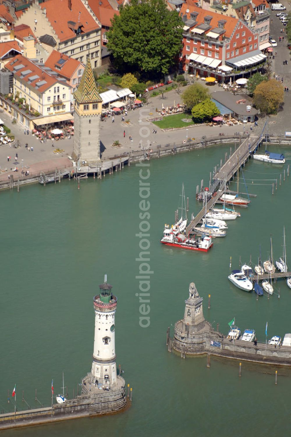 Aerial image Lindau - Blick auf die Hafeneinfahrt der Lindau Insel am Bodensee. Die Hafeneinfahrt an der Lindau Insel ist von einem Leuchtturm und dem Bayerischen Löwen begrenzt. Der Mangturm wurde um 1200 als Leuchtturm erbaut und war der Turm der ehemaligen Stadtbefestigung. Als besonderer Hingucker dient hier das bunte Dach, welches aus dem 19. Jhd. stammt. Seinen Namen hat er durch das ehemalige Tuch- und Manghaus, dass sich dort in der Nähe befand. Kontakt: Tourist-Information, Ludwigstraße 68, 88131 Lindau, Te??????????????????????????????????????????????????????????????????????????