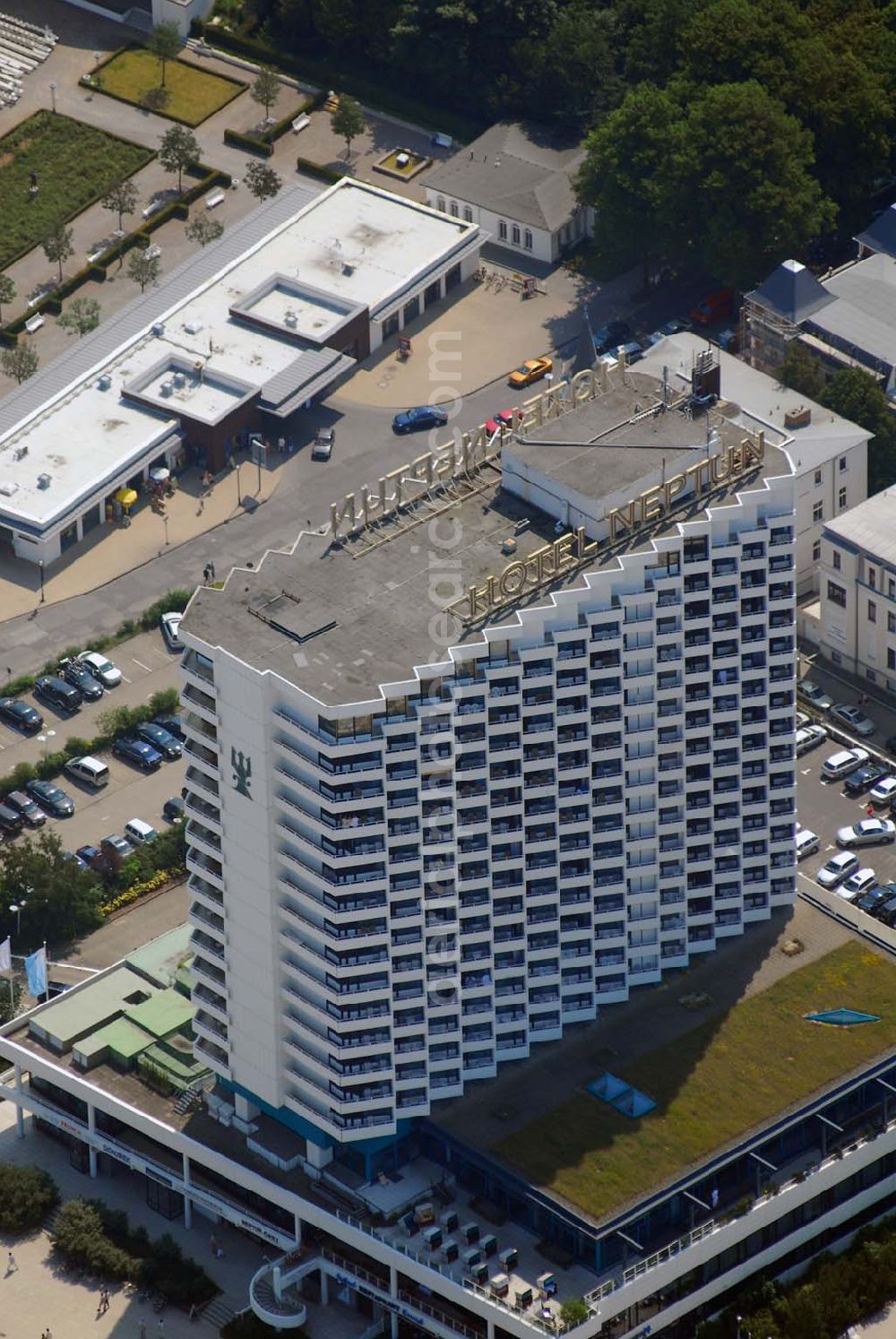 Warnemünde from above - Blick auf das Hotel Neptun, ein direkt am Strand der Ostsee gelegenes 5-Sterne-Hotel im Ostseebad Warnemünde, das 1971 den Betrieb aufnahm. Das Hotel mit 338 Zimmern und dem ersten zertifizierten Thalassozentrum Deutschlandes gehört als „Wellness-Hotel“ zur Arkona AG, einer 100%igen Tochter der Deutschen Seereederei Rostock (DSR). Das ehem.Wohnungsbaukombinat Rostock und das schwedische Unternehmen SIAB errichteten von 1969 bis 1971 den 64 Meter hohen Betonklotz, der im Frühjahr 1971 eröffnet wurde. Die Architekten hatten den Bau so geplant, dass alle der rund 350 Zimmer mit Meeresblick waren. Neben den einheimischen Urlaubern übernachteten auch Geschäftsleute aus dem Westen gern in dem Prestige-Objekt. Hinzu kamen Staatsgäste wie Fidel Castro, aber auch westdeutsche Politiker wie Uwe Barschel und Willy Brandt. Für die Staatssicherheit der DDR eine gute Gelegenheit Informationen zu sammeln.