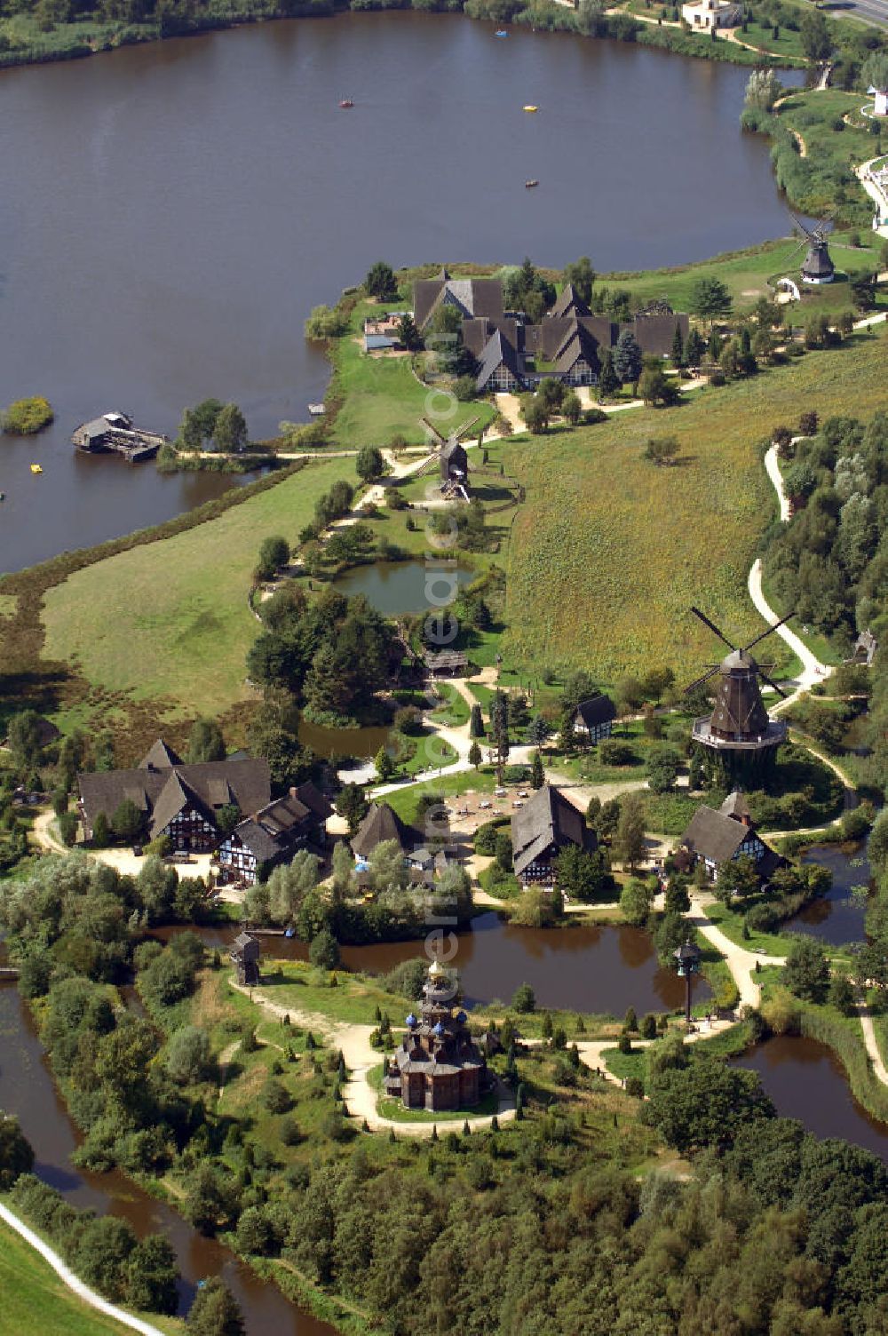 Aerial photograph Gifhorn - Blick auf das Internationale Mühlenmuseum Gifhorn mit Mühlensee. Das Internationale Mühlenmuseum Gifhorn ist eine Einrichtung, die europaweit einzigartig ist. Das Freigelände des Museums ist ca. 16 ha groß. Auf diesem Gelände befinden sich derzeit 16 originale und originalgetreu nachgebaute Mühlen aus insgesamt 12 verschiedenen Ländern. Auch historische Gegenstände aus dem Mühlen- und Müllereiwesen sind auf dem ganzen Gelände ausgestellt. Das Museum wurde 1980 eröffnet. Durch Schwemmbaggern u. v. m. wurde das Gelände modeliert. Dabei entstand unter an derem auch der 5 ha große Mühlensee. Der See dient zur Wasserregulierung der Ise und als Rückhaltebecken für den Hochwasserschutz. Kontakt: Internationales Wind- und Wassermühlen-Museum, Bromer Straße 2, 38518 Gifhorn, Tel.: +49(0)537155 466, Fax: +49(0)537155 640