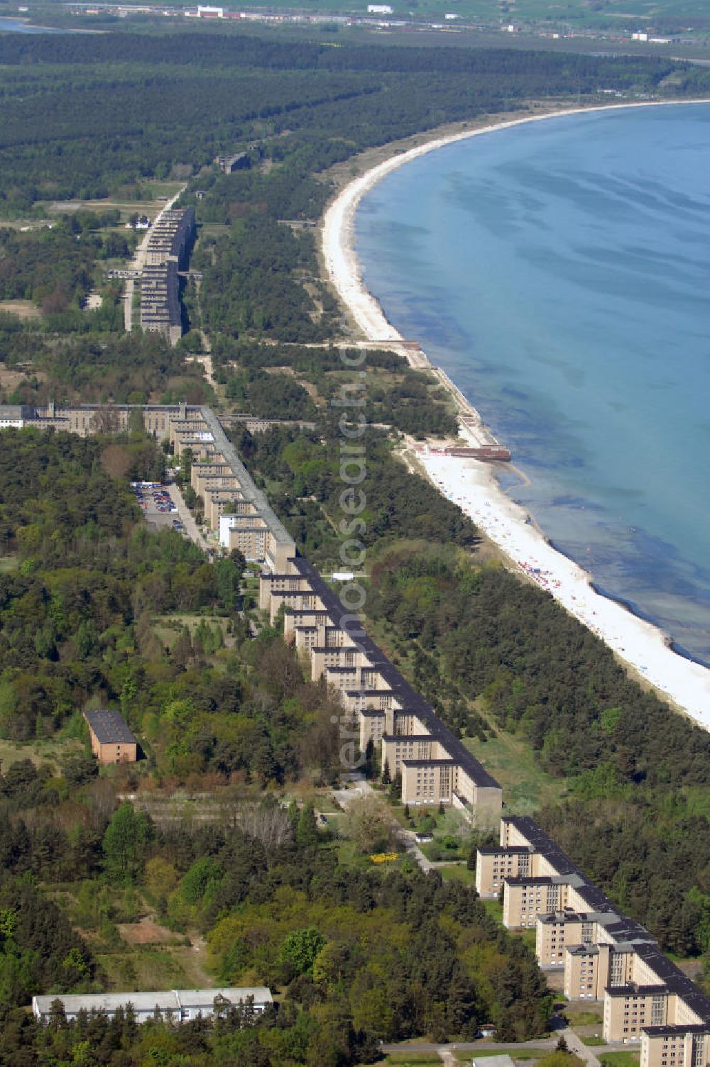 Ostseebad Prora from above - Blick auf den „Koloss von Prora“ die 18m-Modellanlage KdF-Seebad Prora. Am 2. Mai 1936 fand die Grundsteinlegung des 1. von insgesamt 5 an der Nord und Ostseeküste geplanten Seebäder der 20.000 in Pora auf Rügen statt. Im November 1936 begannen 9 Baukonzerne und 48 Baufirmen mit ca. 5000 Arbeiter die Bauausführung, im Oktober 1938 konnte bereits Richtfest für das erste 500 m lange Unterkunftshaus gefeiert werden. Mit Kriegsbeginn 1939 wurden die Arbeiten auf der riesigen Großbaustelle stillgelegt. Nach 1945 wurden Teile des rohbauferigen KdF - Seebades demontiert und Abschnitte des Nordflügels von sowjetischen Truppen gesprengt. In den 50er Jahren übernahm die NVA der DDR das riesige Areal und baute es zu einem Militärstandort aus, etwa 10000 Soldaten und Offiziere waren ständig bis zur Auflösung 1990 in Prora kaserniert. Heute sind in dem historischen Gebäudekomplex u.a. folgende Einrichtungen untergebracht: Dokumentationszentrum der Stiftung NEUE KULTUR, das Museum zum Anfassen, KulturKunststatt Prora und die Grafik-Galerie.