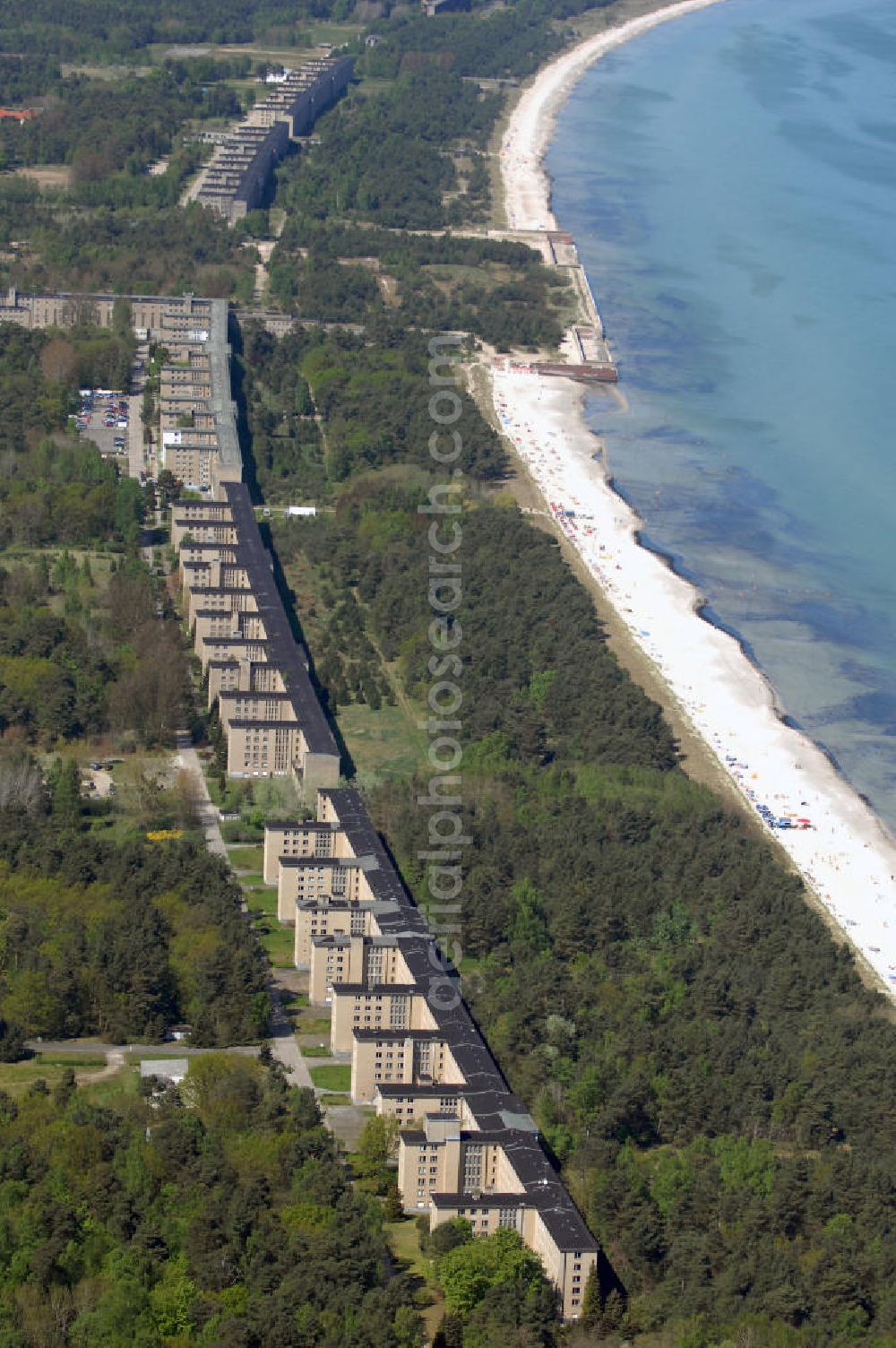 Aerial image Ostseebad Prora - Blick auf den „Koloss von Prora“ die 18m-Modellanlage KdF-Seebad Prora. Am 2. Mai 1936 fand die Grundsteinlegung des 1. von insgesamt 5 an der Nord und Ostseeküste geplanten Seebäder der 20.000 in Pora auf Rügen statt. Im November 1936 begannen 9 Baukonzerne und 48 Baufirmen mit ca. 5000 Arbeiter die Bauausführung, im Oktober 1938 konnte bereits Richtfest für das erste 500 m lange Unterkunftshaus gefeiert werden. Mit Kriegsbeginn 1939 wurden die Arbeiten auf der riesigen Großbaustelle stillgelegt. Nach 1945 wurden Teile des rohbauferigen KdF - Seebades demontiert und Abschnitte des Nordflügels von sowjetischen Truppen gesprengt. In den 50er Jahren übernahm die NVA der DDR das riesige Areal und baute es zu einem Militärstandort aus, etwa 10000 Soldaten und Offiziere waren ständig bis zur Auflösung 1990 in Prora kaserniert. Heute sind in dem historischen Gebäudekomplex u.a. folgende Einrichtungen untergebracht: Dokumentationszentrum der Stiftung NEUE KULTUR, das Museum zum Anfassen, KulturKunststatt Prora und die Grafik-Galerie.