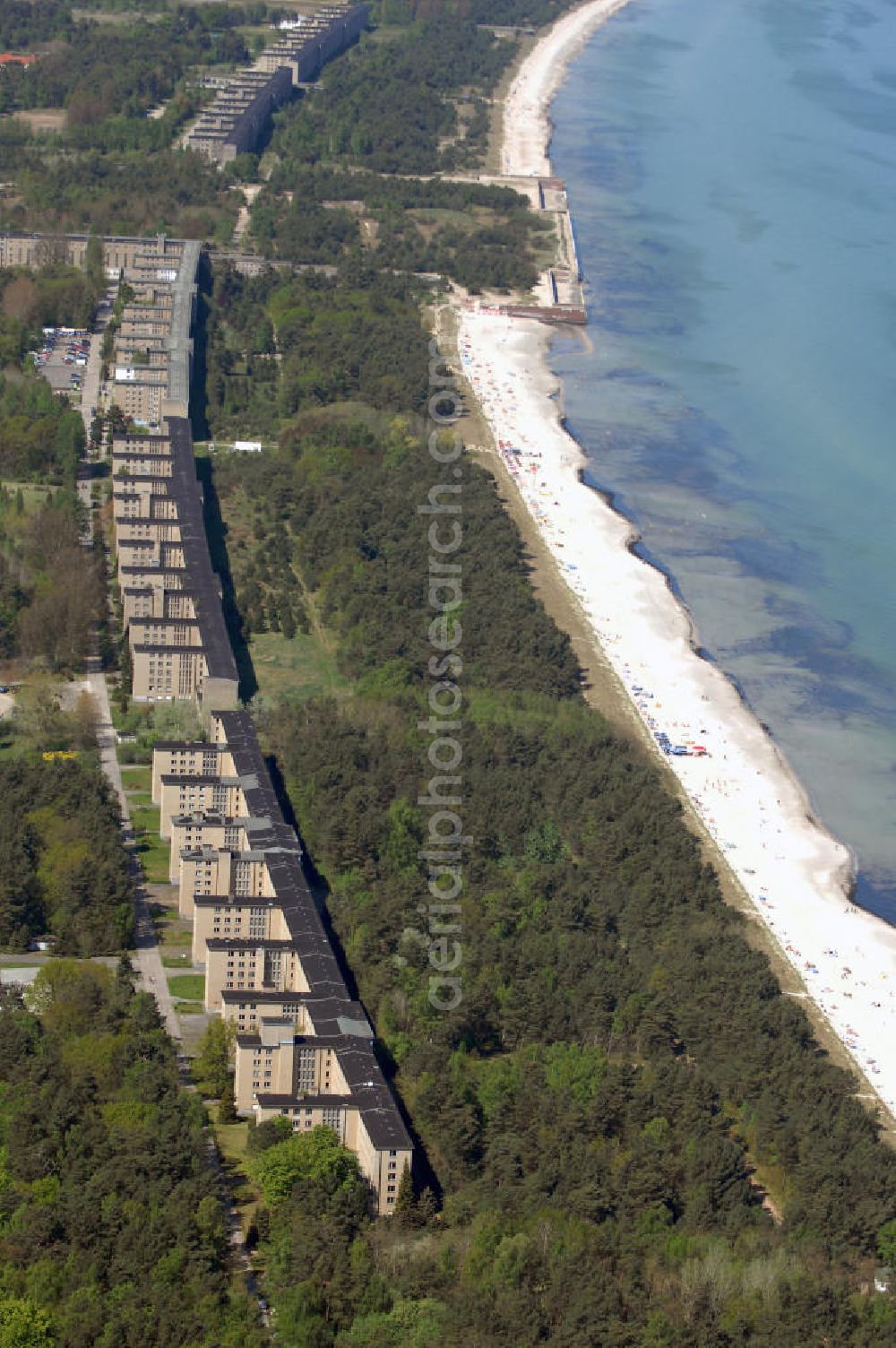 Ostseebad Prora from above - Blick auf den „Koloss von Prora“ die 18m-Modellanlage KdF-Seebad Prora. Am 2. Mai 1936 fand die Grundsteinlegung des 1. von insgesamt 5 an der Nord und Ostseeküste geplanten Seebäder der 20.000 in Pora auf Rügen statt. Im November 1936 begannen 9 Baukonzerne und 48 Baufirmen mit ca. 5000 Arbeiter die Bauausführung, im Oktober 1938 konnte bereits Richtfest für das erste 500 m lange Unterkunftshaus gefeiert werden. Mit Kriegsbeginn 1939 wurden die Arbeiten auf der riesigen Großbaustelle stillgelegt. Nach 1945 wurden Teile des rohbauferigen KdF - Seebades demontiert und Abschnitte des Nordflügels von sowjetischen Truppen gesprengt. In den 50er Jahren übernahm die NVA der DDR das riesige Areal und baute es zu einem Militärstandort aus, etwa 10000 Soldaten und Offiziere waren ständig bis zur Auflösung 1990 in Prora kaserniert. Heute sind in dem historischen Gebäudekomplex u.a. folgende Einrichtungen untergebracht: Dokumentationszentrum der Stiftung NEUE KULTUR, das Museum zum Anfassen, KulturKunststatt Prora und die Grafik-Galerie.