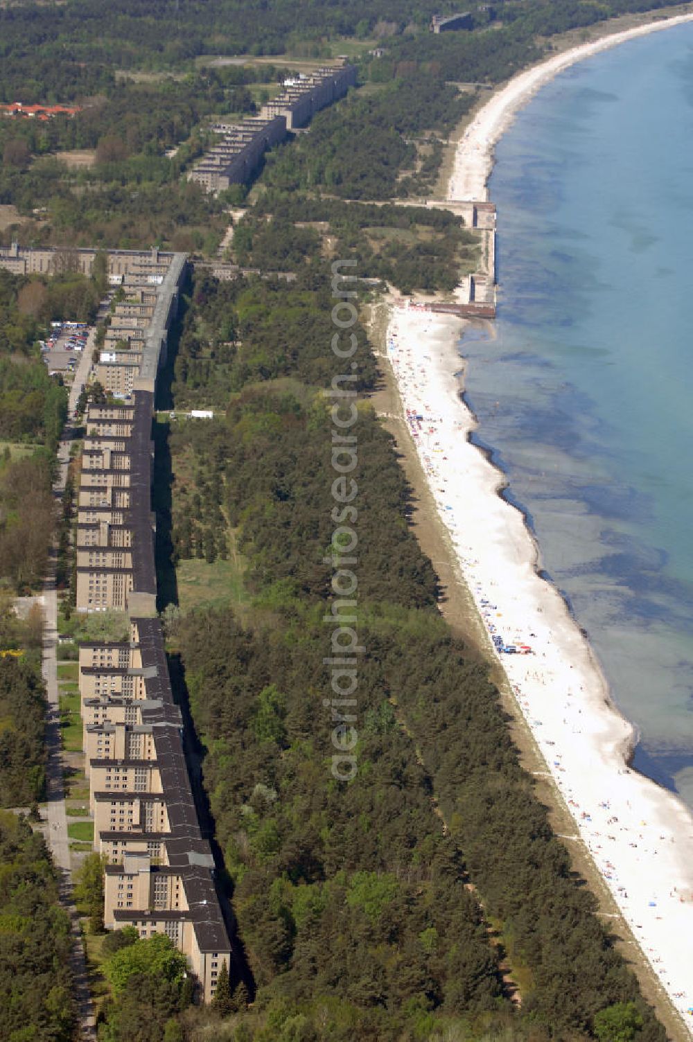 Aerial image Ostseebad Prora - Blick auf den „Koloss von Prora“ die 18m-Modellanlage KdF-Seebad Prora. Am 2. Mai 1936 fand die Grundsteinlegung des 1. von insgesamt 5 an der Nord und Ostseeküste geplanten Seebäder der 20.000 in Pora auf Rügen statt. Im November 1936 begannen 9 Baukonzerne und 48 Baufirmen mit ca. 5000 Arbeiter die Bauausführung, im Oktober 1938 konnte bereits Richtfest für das erste 500 m lange Unterkunftshaus gefeiert werden. Mit Kriegsbeginn 1939 wurden die Arbeiten auf der riesigen Großbaustelle stillgelegt. Nach 1945 wurden Teile des rohbauferigen KdF - Seebades demontiert und Abschnitte des Nordflügels von sowjetischen Truppen gesprengt. In den 50er Jahren übernahm die NVA der DDR das riesige Areal und baute es zu einem Militärstandort aus, etwa 10000 Soldaten und Offiziere waren ständig bis zur Auflösung 1990 in Prora kaserniert. Heute sind in dem historischen Gebäudekomplex u.a. folgende Einrichtungen untergebracht: Dokumentationszentrum der Stiftung NEUE KULTUR, das Museum zum Anfassen, KulturKunststatt Prora und die Grafik-Galerie.