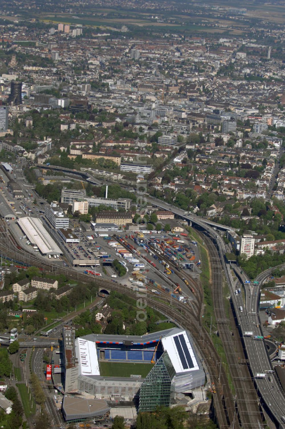 Aerial photograph Basel - Blick über die Stadt mit Stadion und Bahnhof. Der St. Jakob-Park (früher St. Jakob-Stadion, lokal Joggeli genannt) ist zur Zeit das grösste Fussballstadion der Schweiz und ist Teil des Sportzentrum St. Jakob. Es ist das Heimstadion des Fussballclub Basel (FCB). Es wurde von den Architekten Herzog & de Meuron von 1999 bis 2001 erstellt und hat ein Fassungsvermögen von 38500 Sitzplätzen. Es ist Austragungsort und Eröffnungsort der Europameisterschaft 2008. Zum St. Jakob-Park gehört auch der neu erbaute St.Jakob Turm mit Glasfassade.